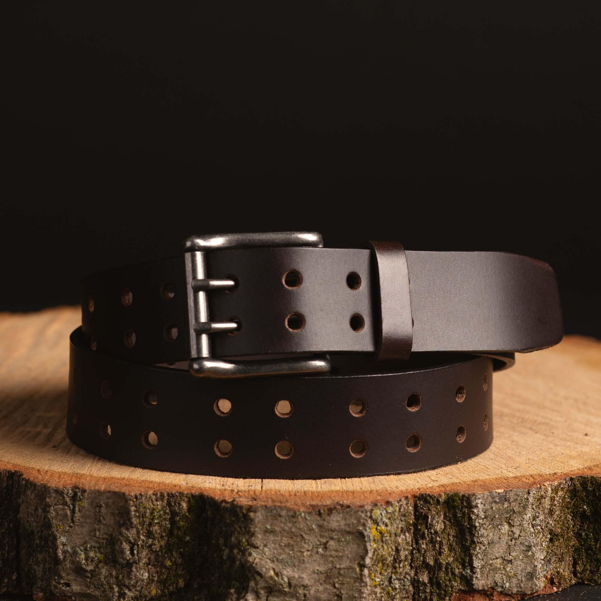 Brown leather belt with punched holes and double prong buckle on wood slice, dark background