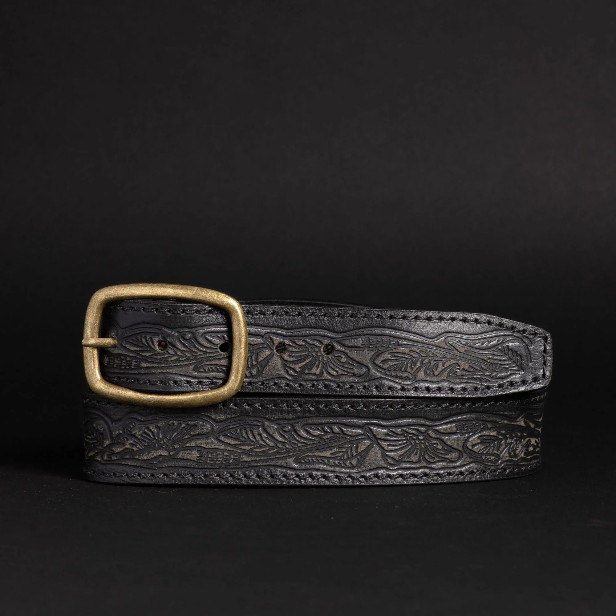Black embossed leather belt with brass buckle on black background