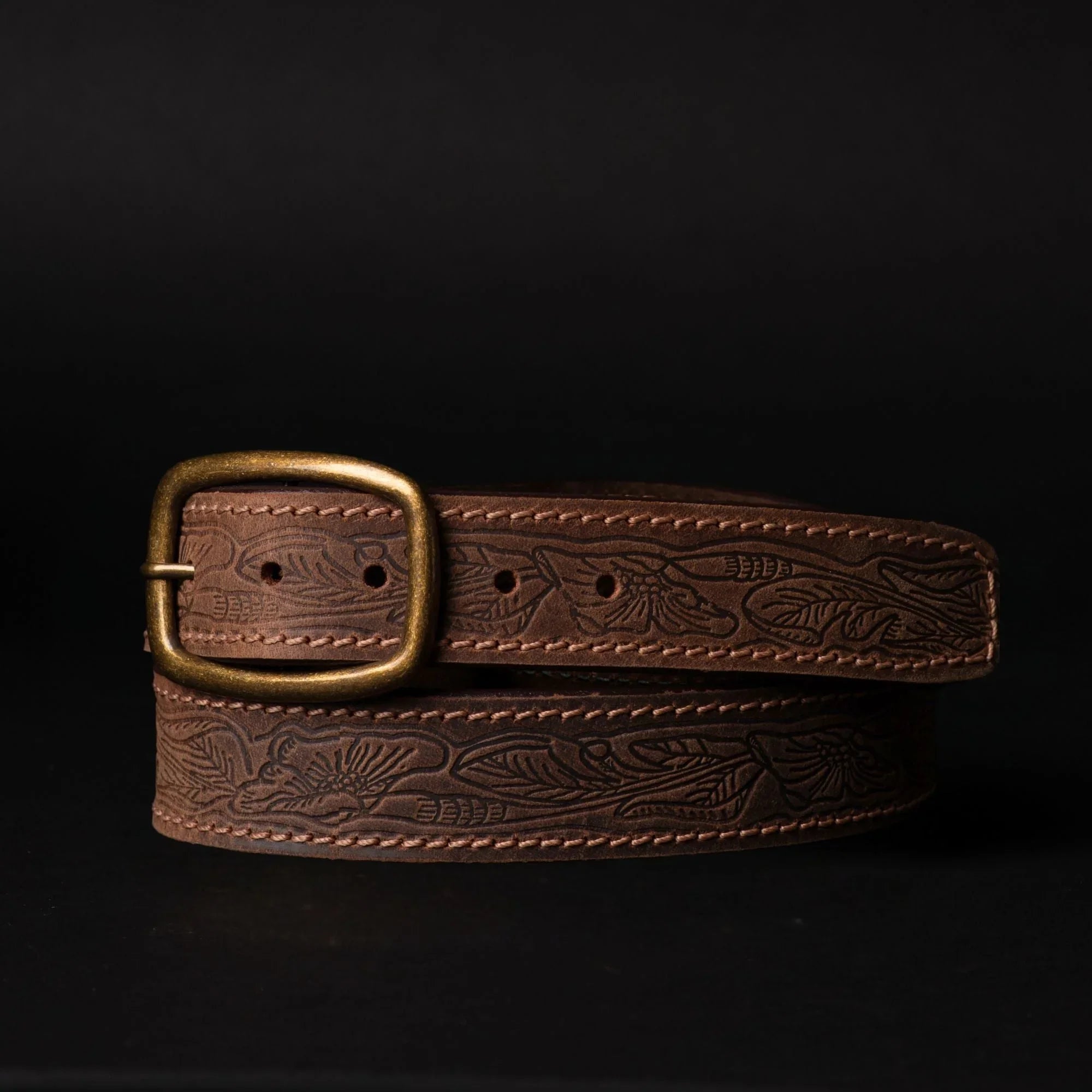 Brown embossed leather belt with brass buckle on black background