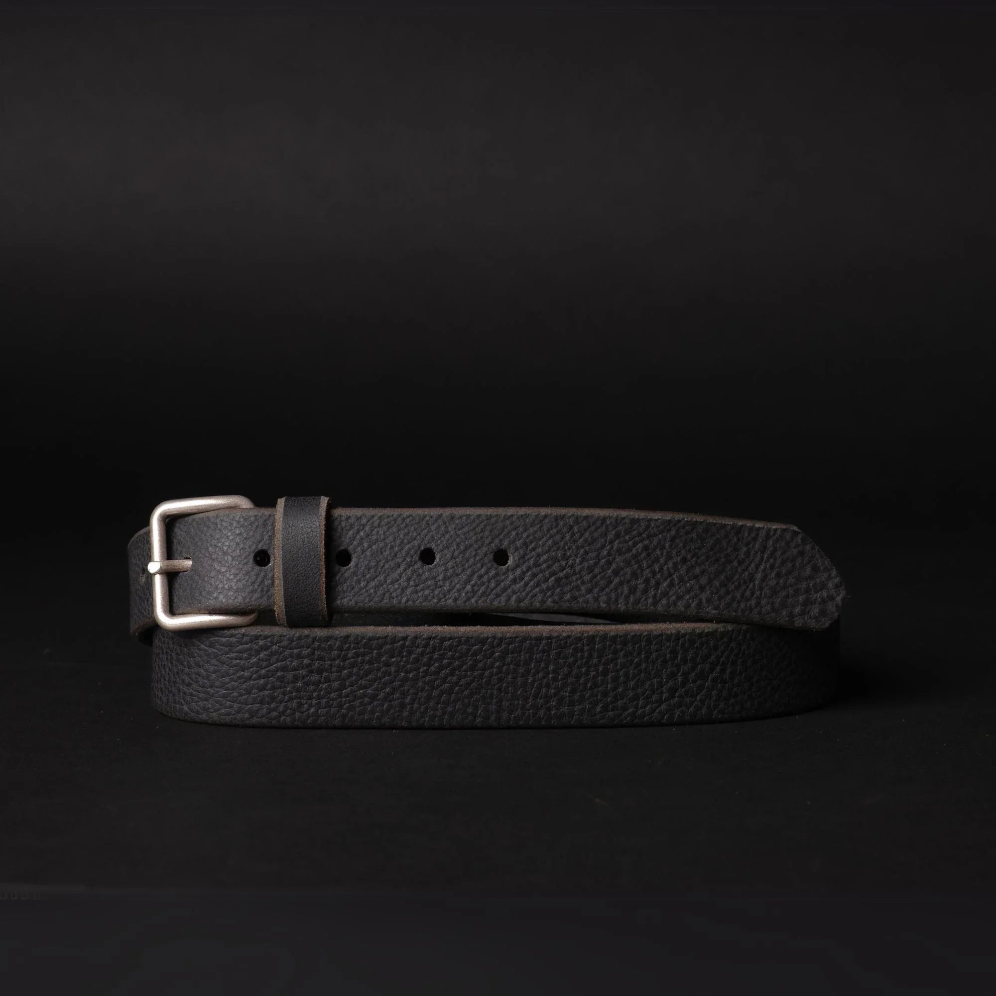 Black leather belt with silver buckle on black background, textured finish