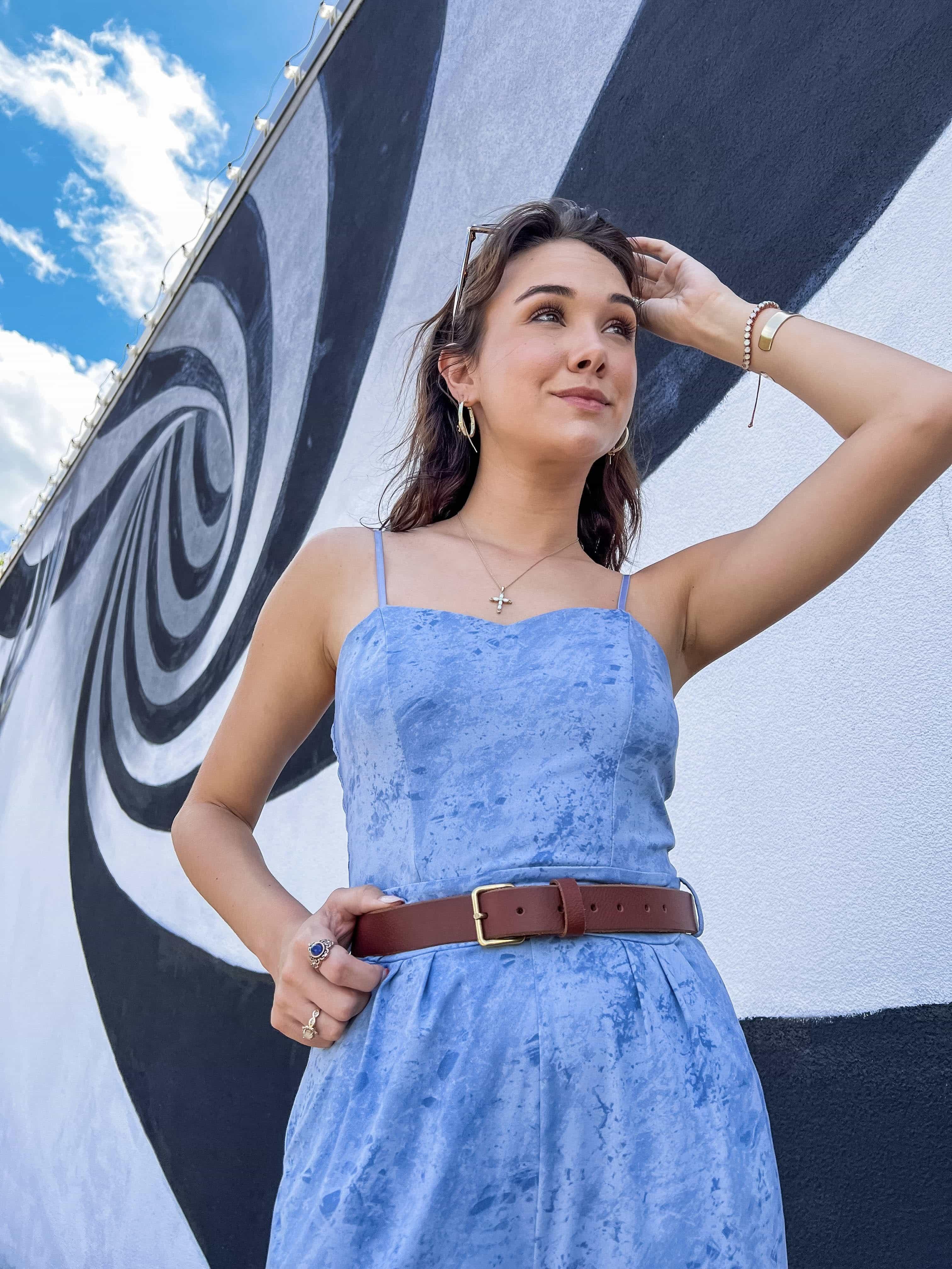 Woman in a light blue dress with brown belt posing by black and white swirl mural outdoors