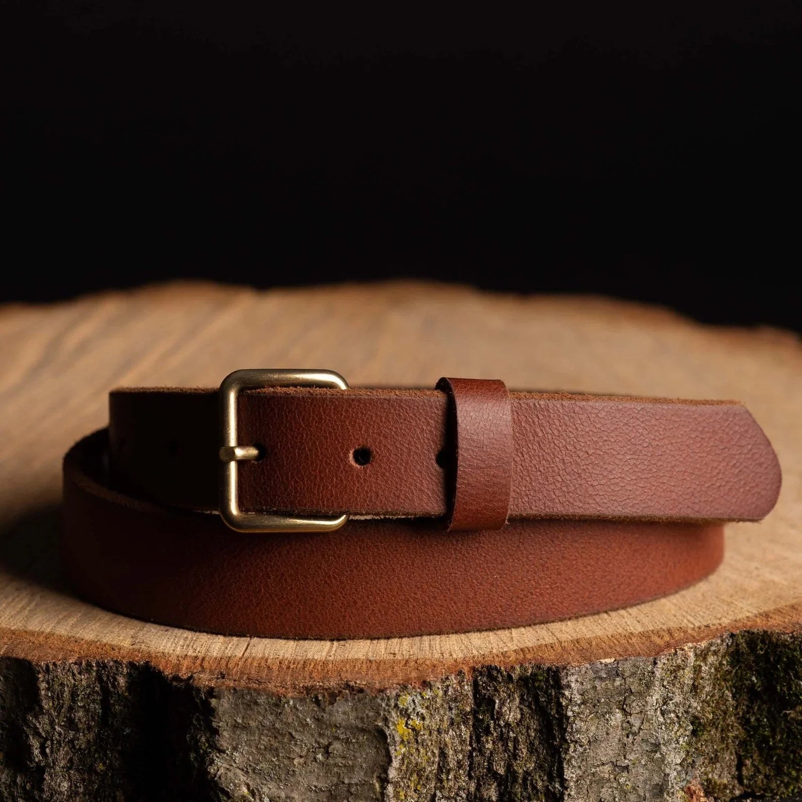 Brown leather belt with brass buckle on wooden surface, rustic men's accessory