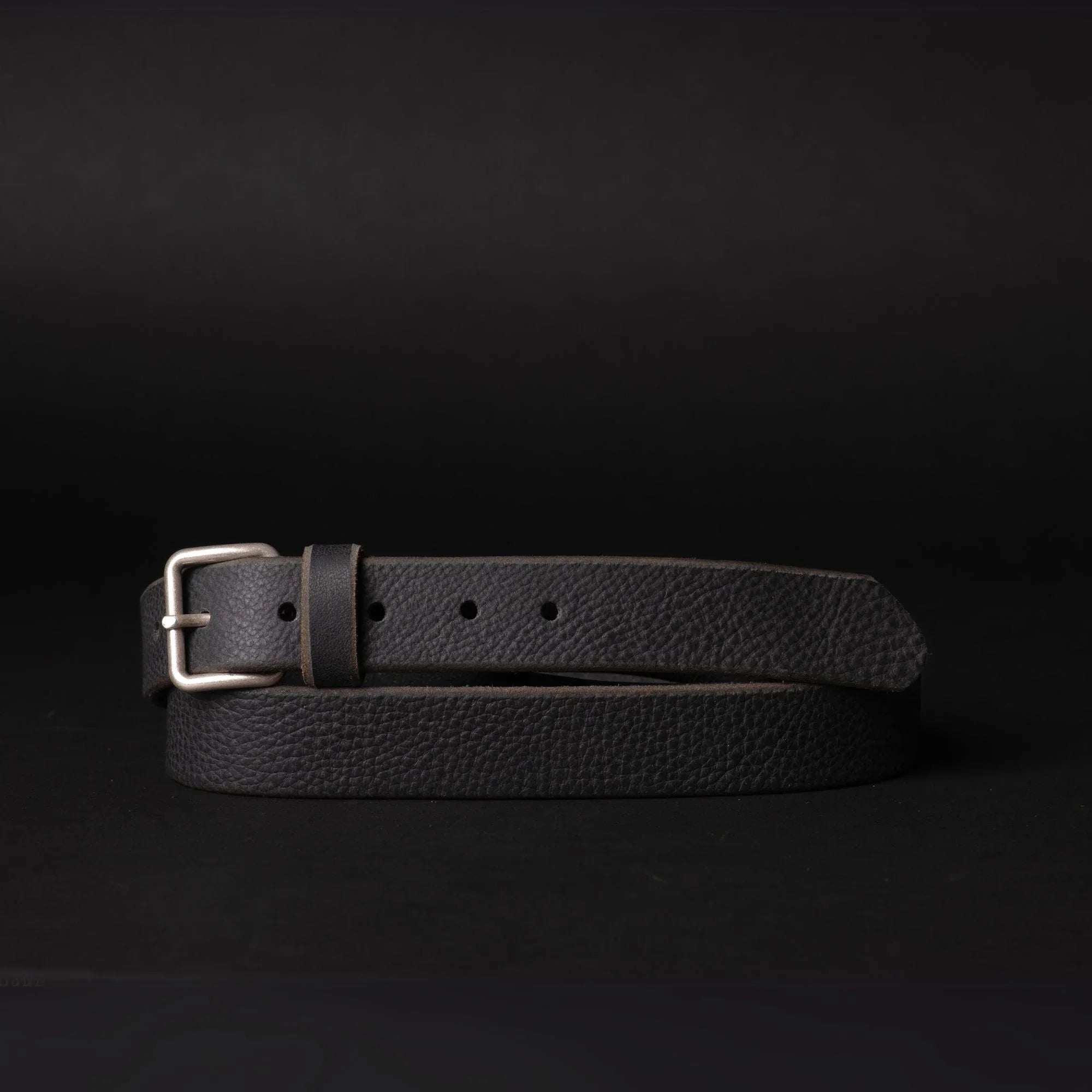 Black leather belt with silver buckle on dark background, minimalist men's accessory