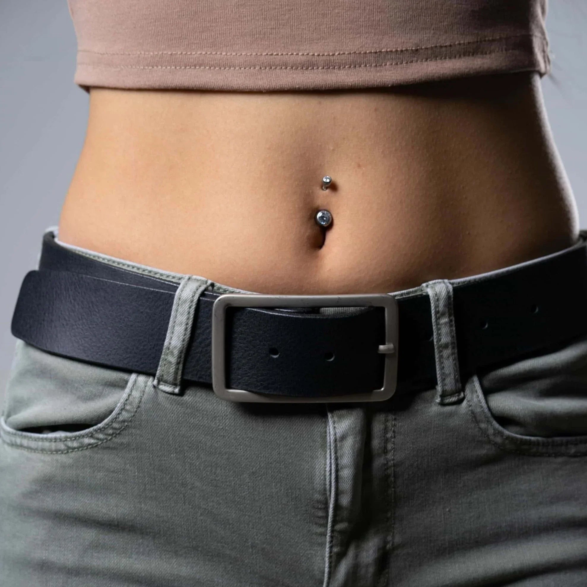 Black leather belt on jeans, closeup of waist with belly button piercing