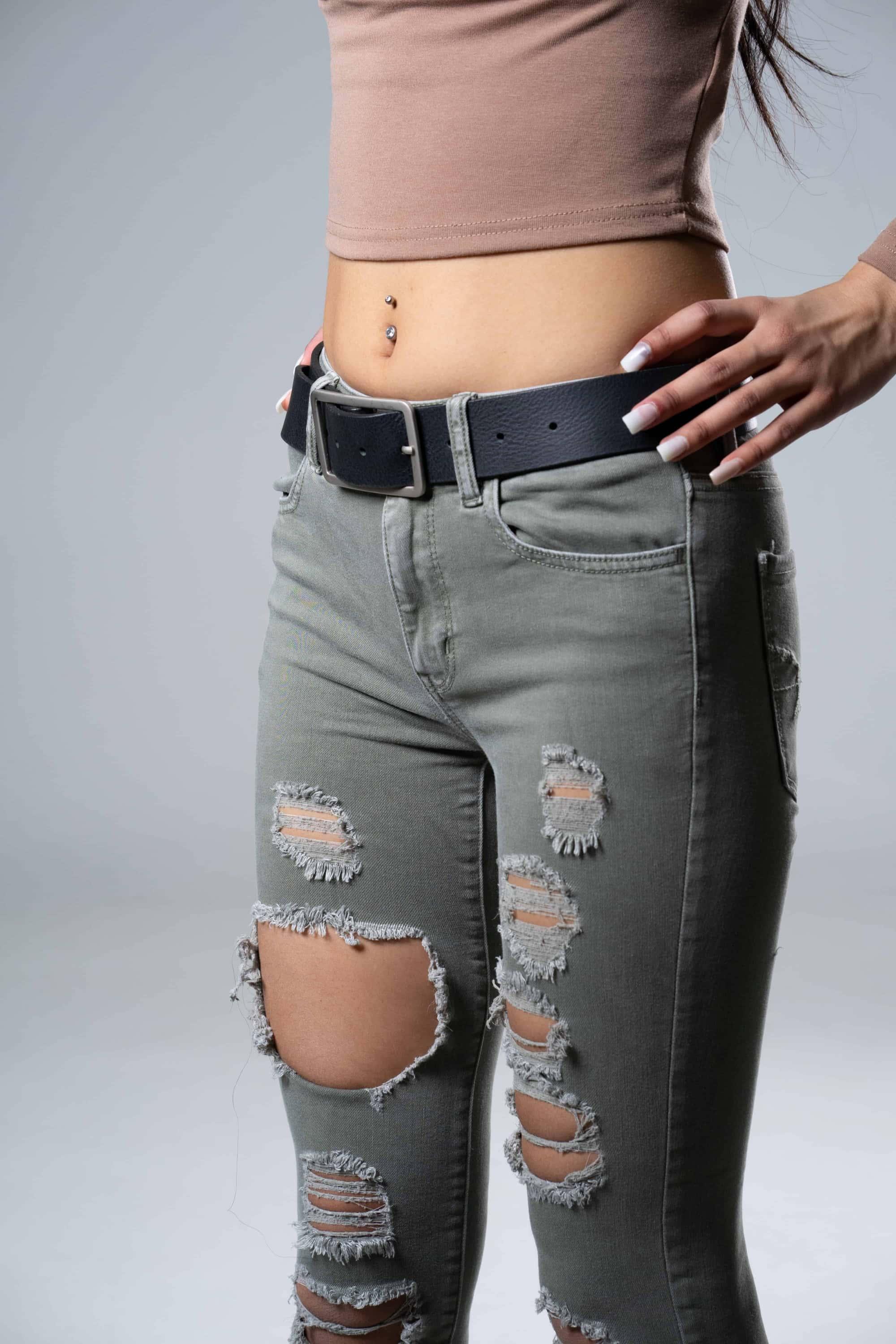 Woman wearing ripped gray jeans, black belt, and crop top, showing belly piercing
