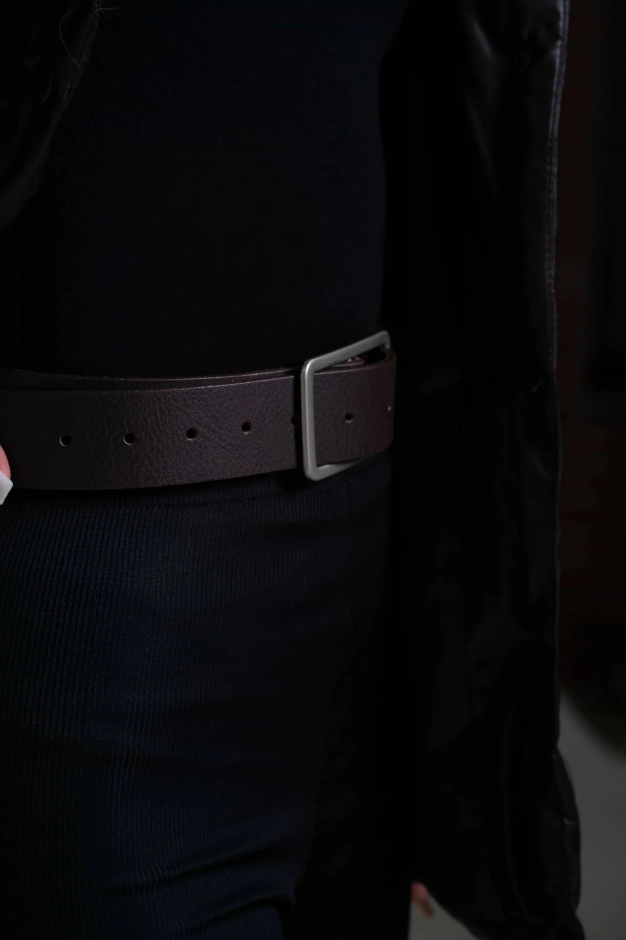Dark brown leather belt with silver buckle on a person wearing black clothing