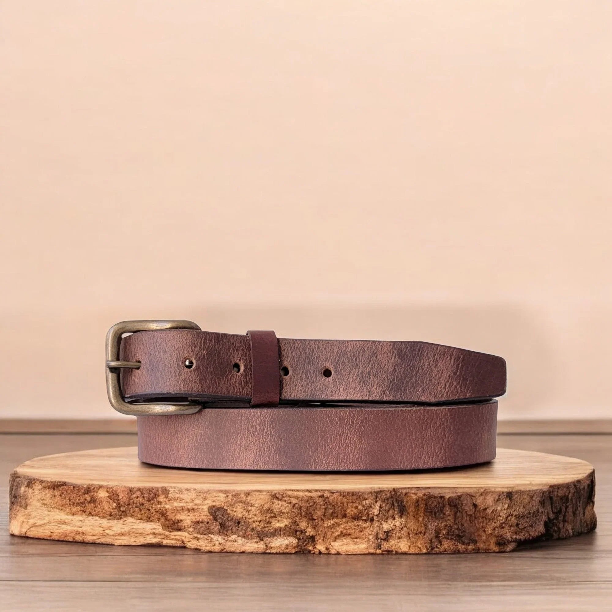 Brown leather belt with brass buckle on wooden display, minimalist background