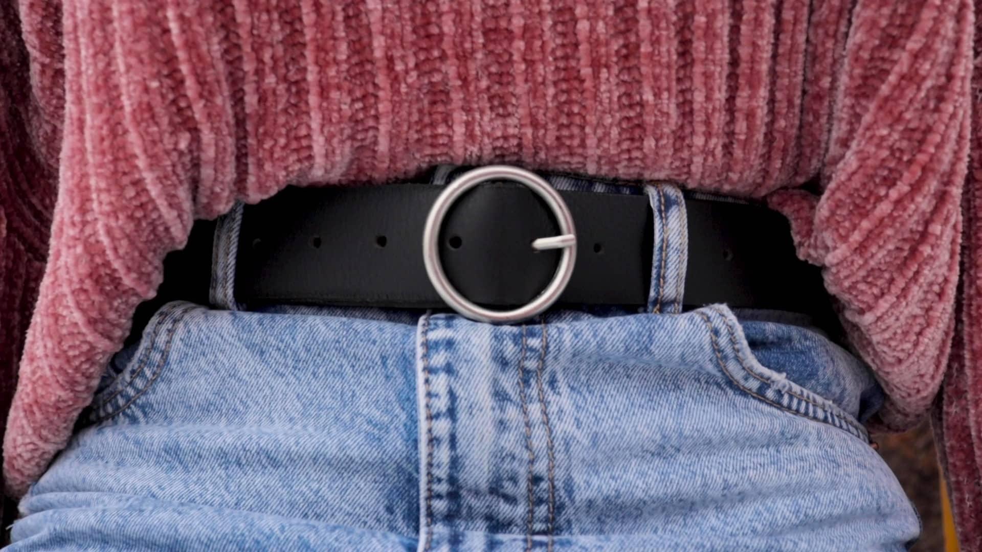 Black round buckle belt on blue jeans with pink textured sweater