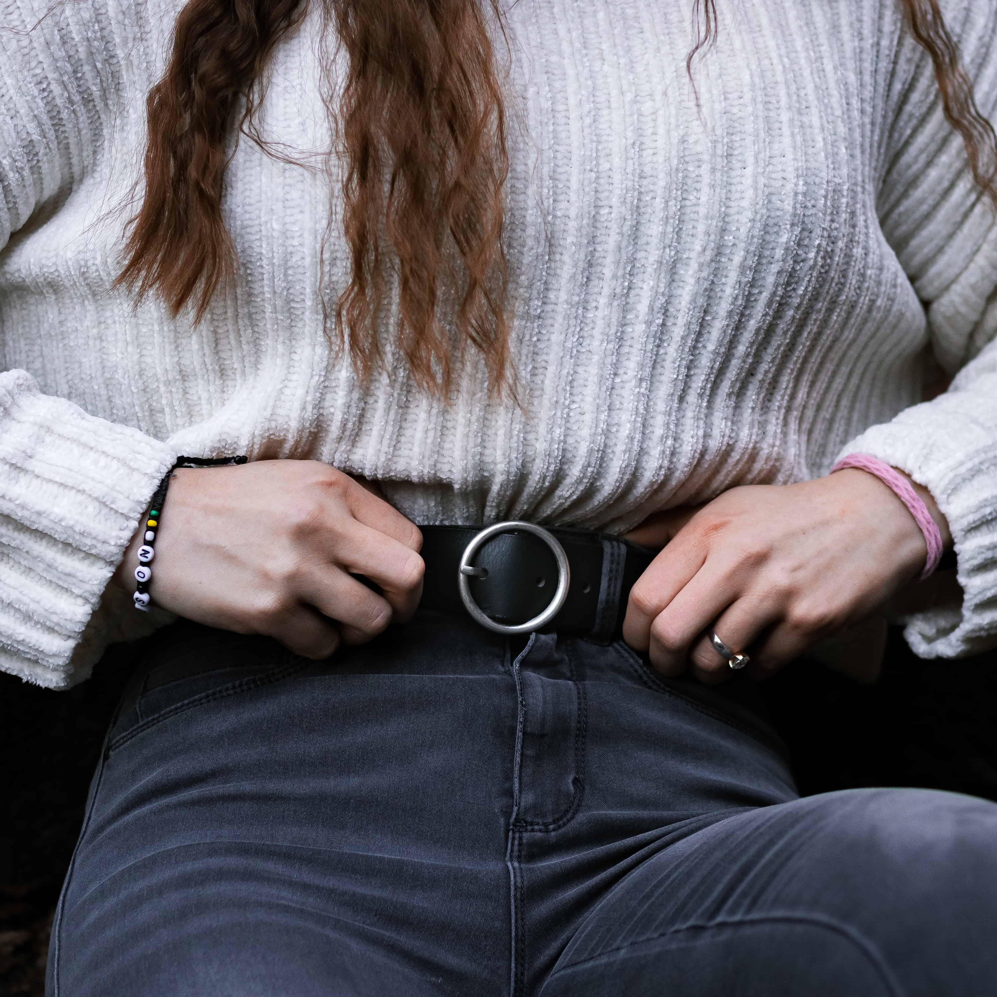 Woman in white ribbed sweater and dark jeans wearing a round buckle black belt