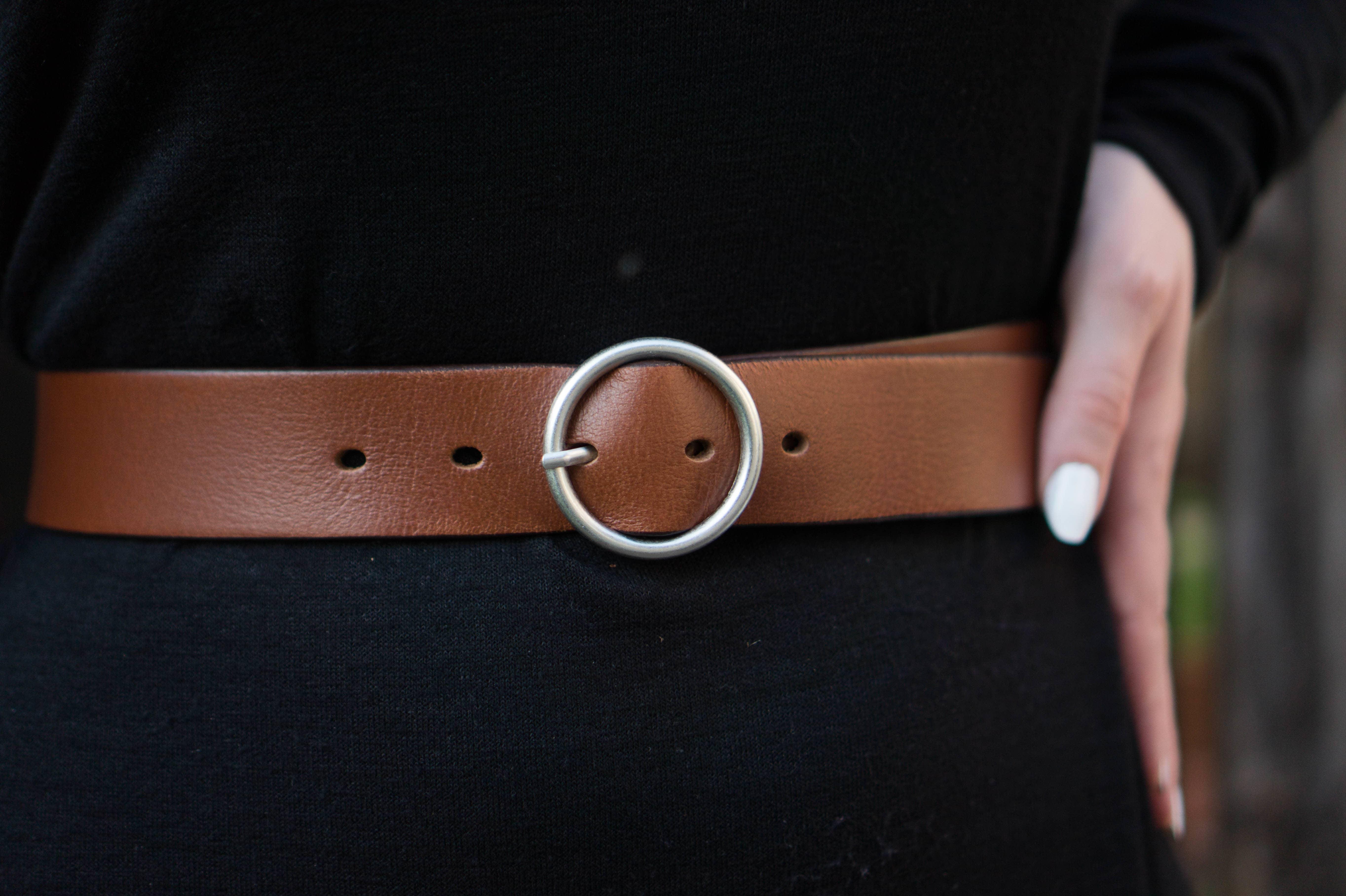 Brown leather belt with silver round buckle on black dress, hand on waist