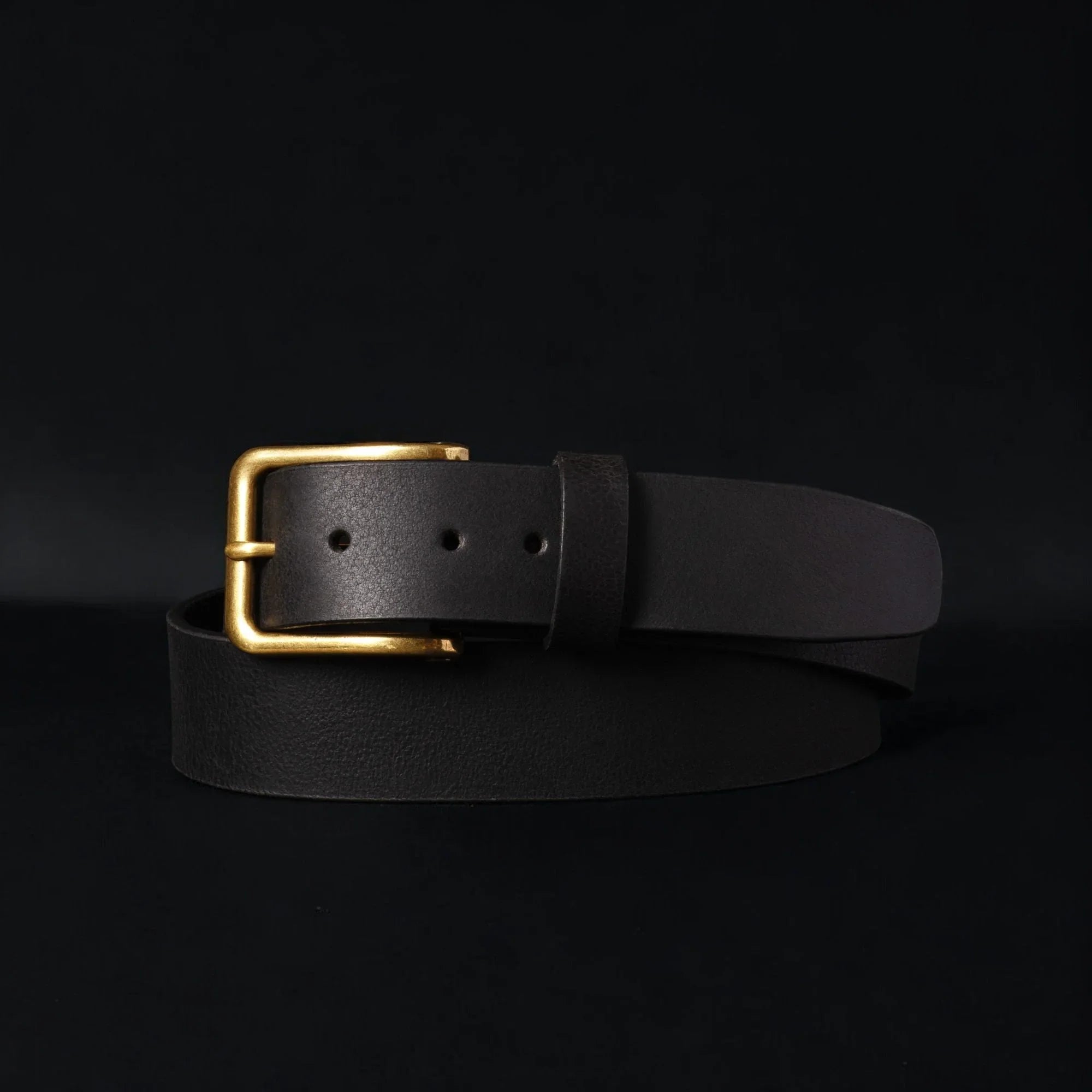Black leather belt with gold buckle on black background