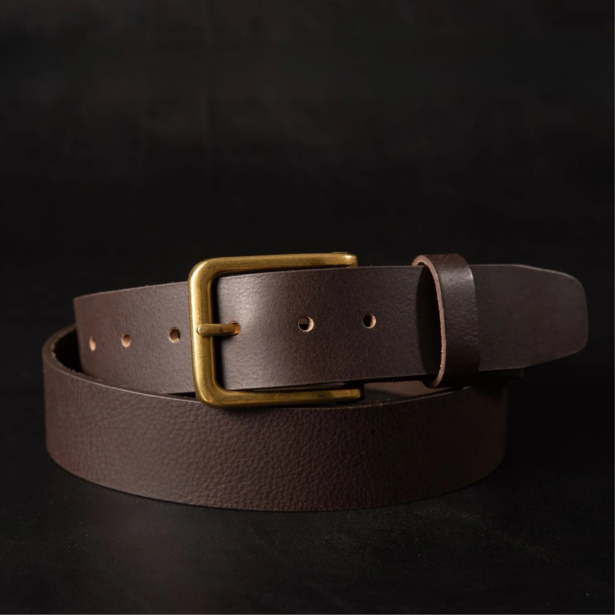 Brown leather belt with brass buckle on dark background