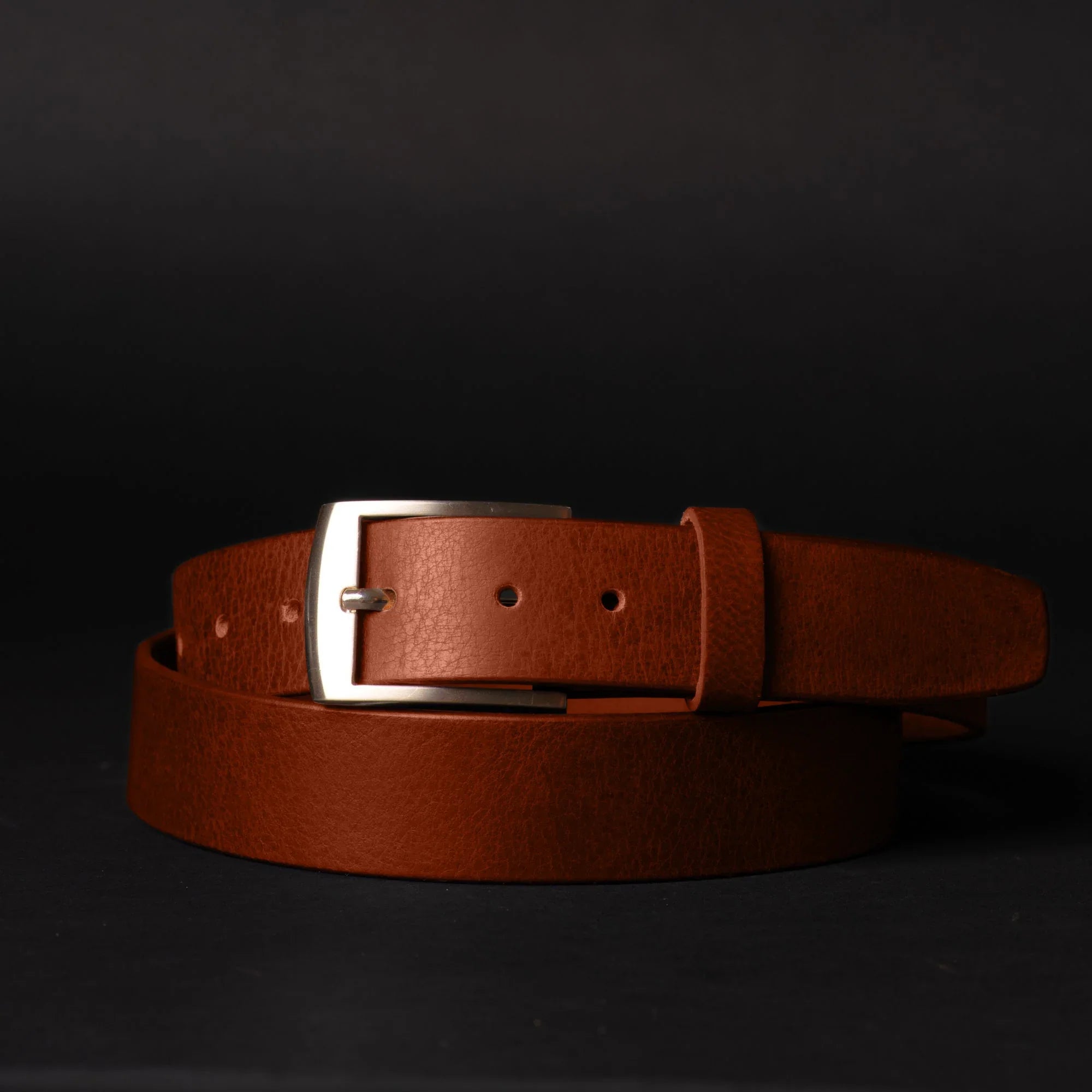 brown leather belt with silver buckle on black background