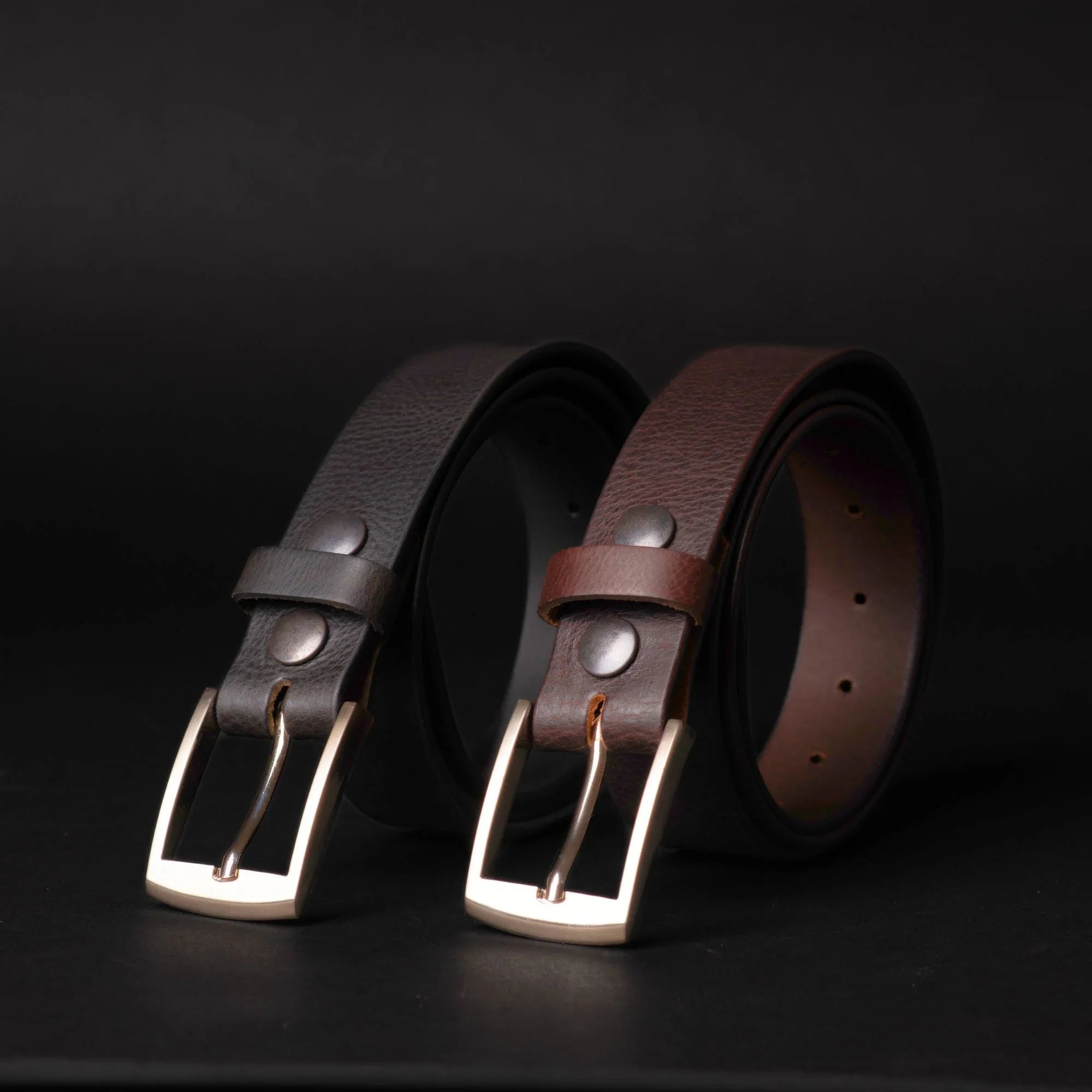 Black and brown leather belts with metal buckles on black background