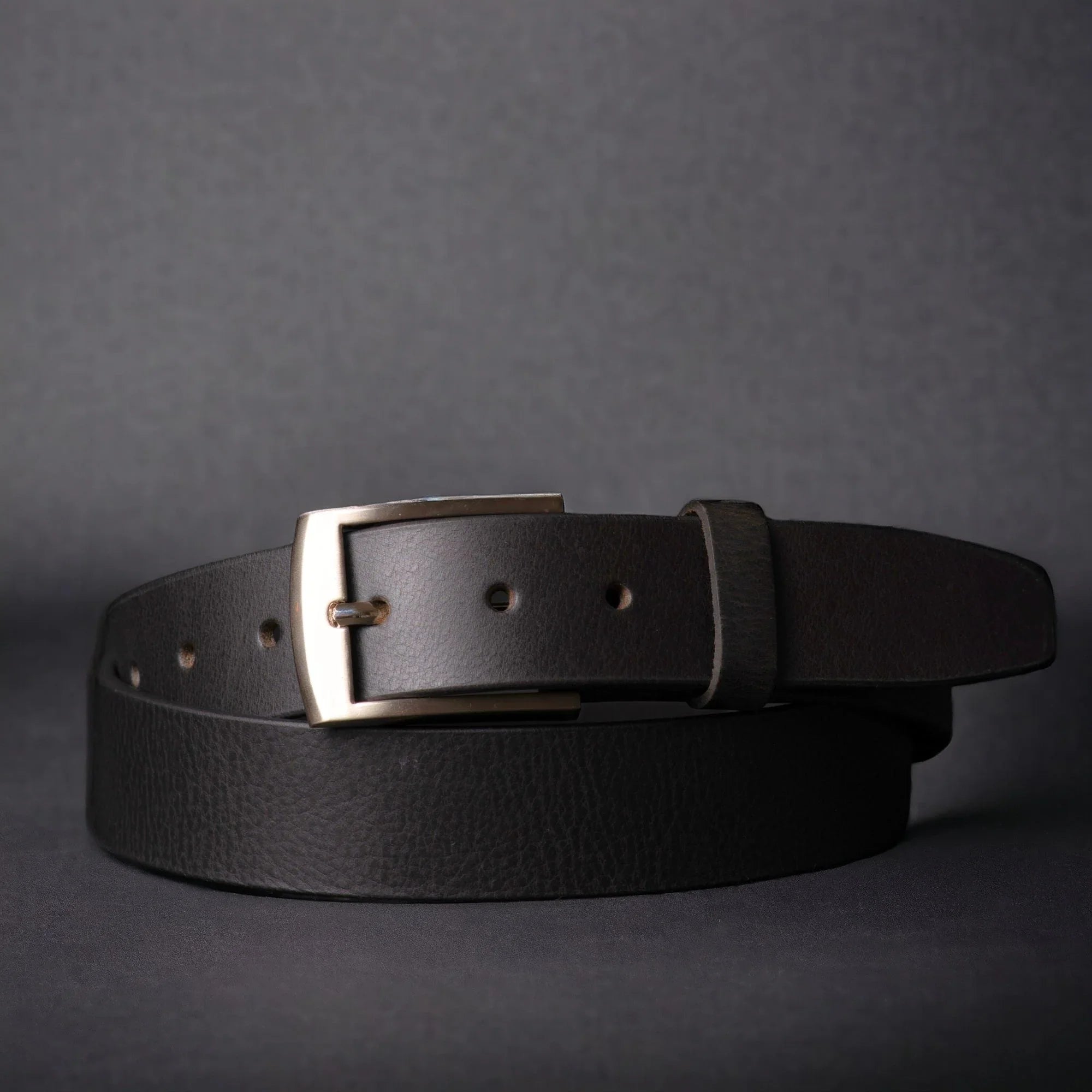 Black leather belt with silver buckle on dark background