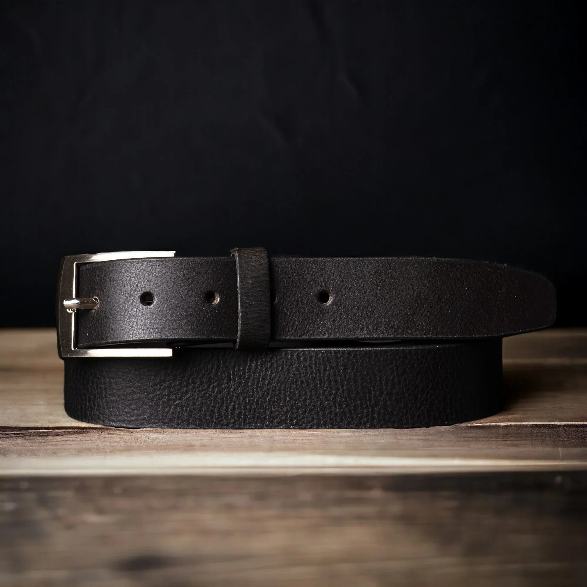 Black leather belt with silver buckle on wooden table, fashion accessory product photo