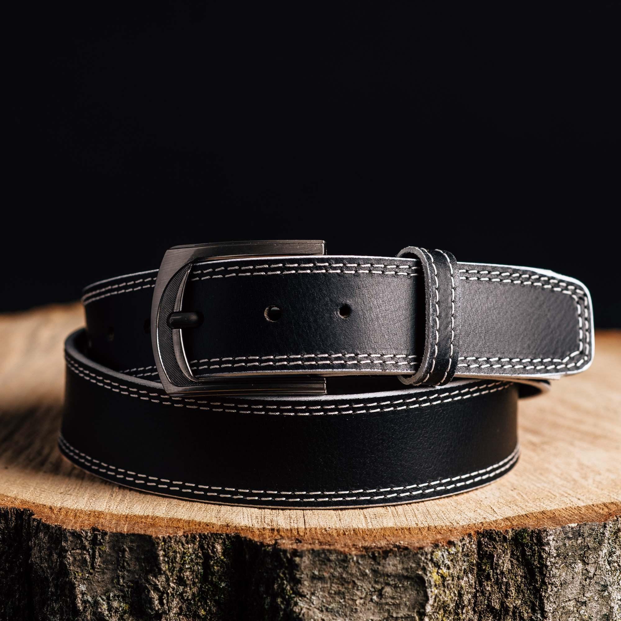 Black leather belt with white stitching and silver buckle on wooden surface