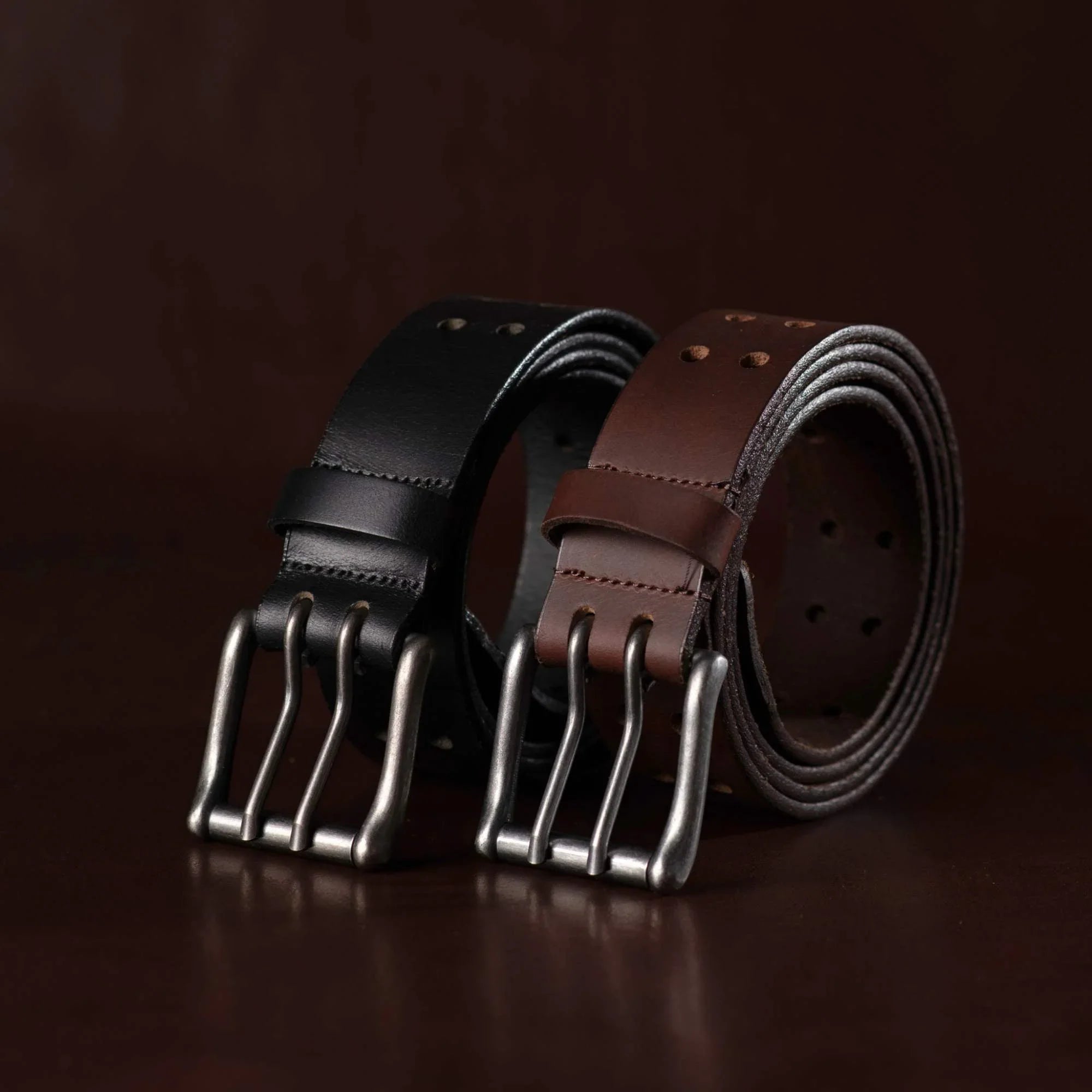 Black and brown leather belts with triple metal buckles on dark background