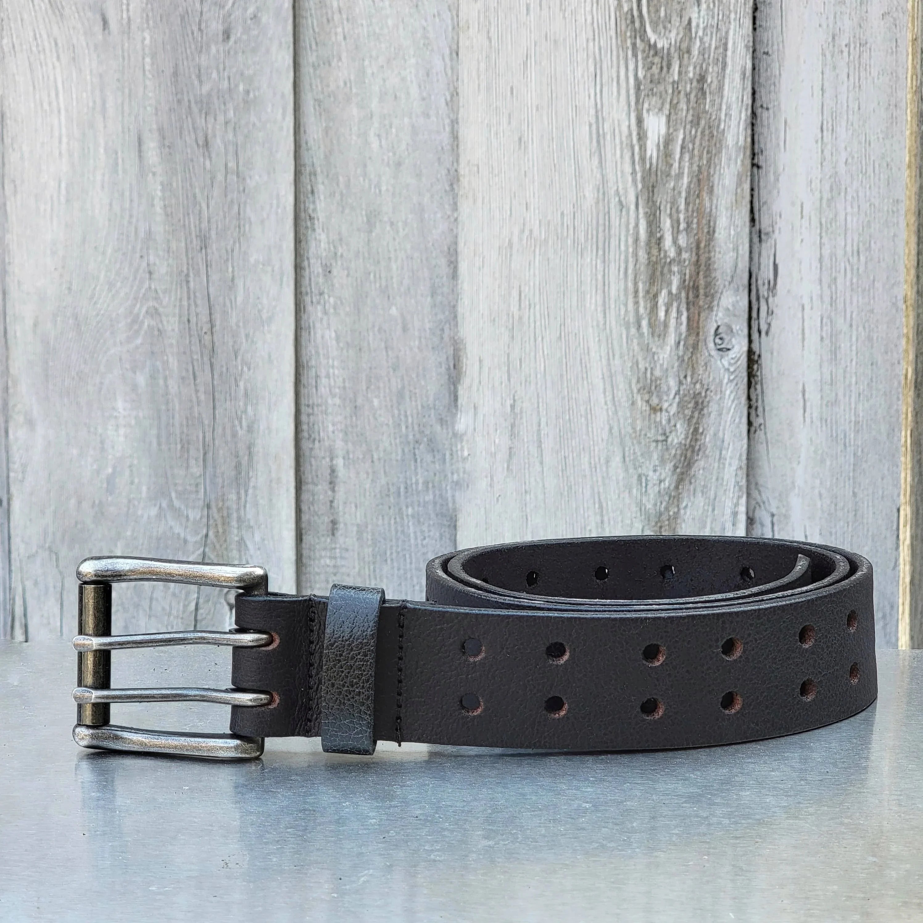 Black leather double prong belt with metal buckle on rustic wood background