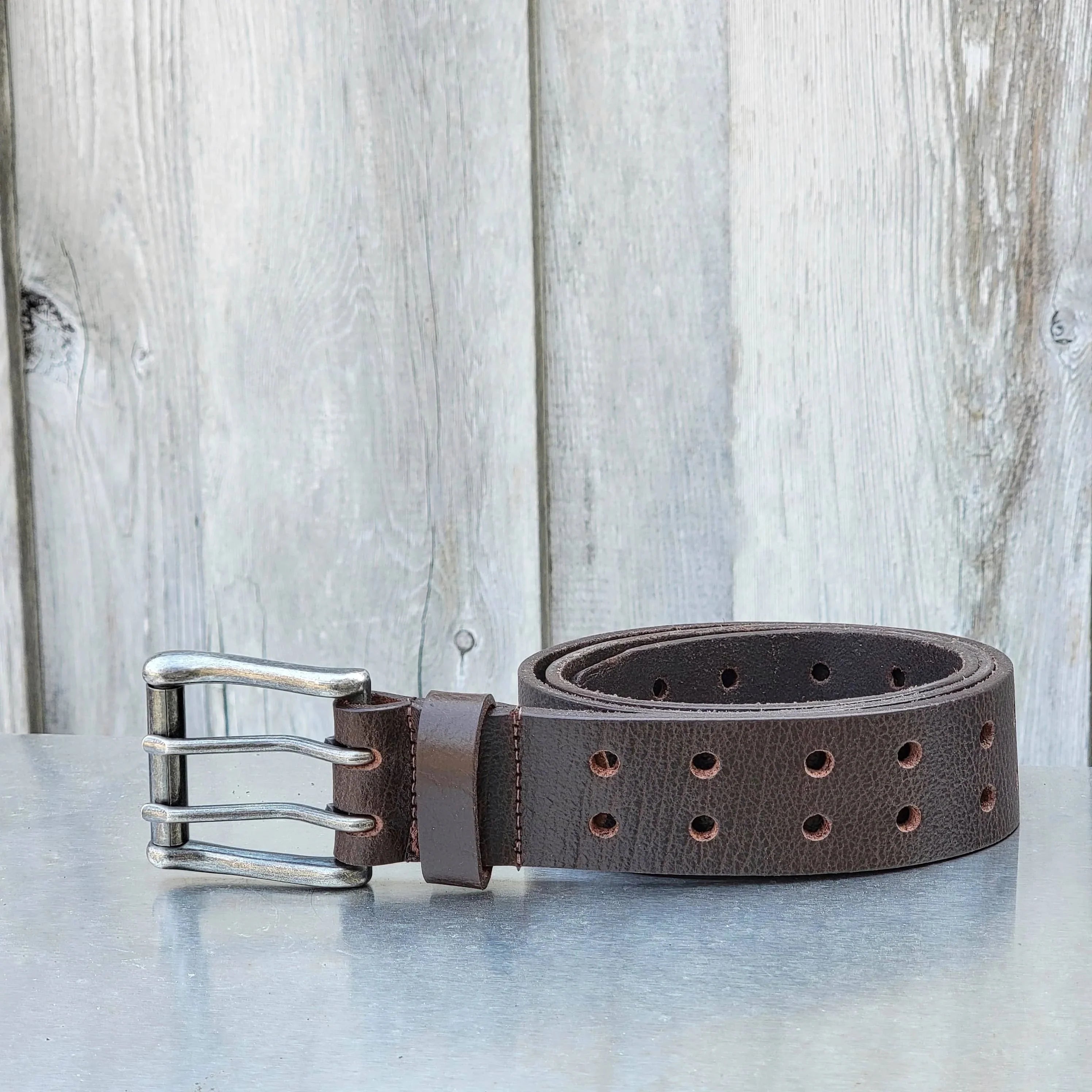 Brown leather triple-prong belt with metal buckle on rustic wood background