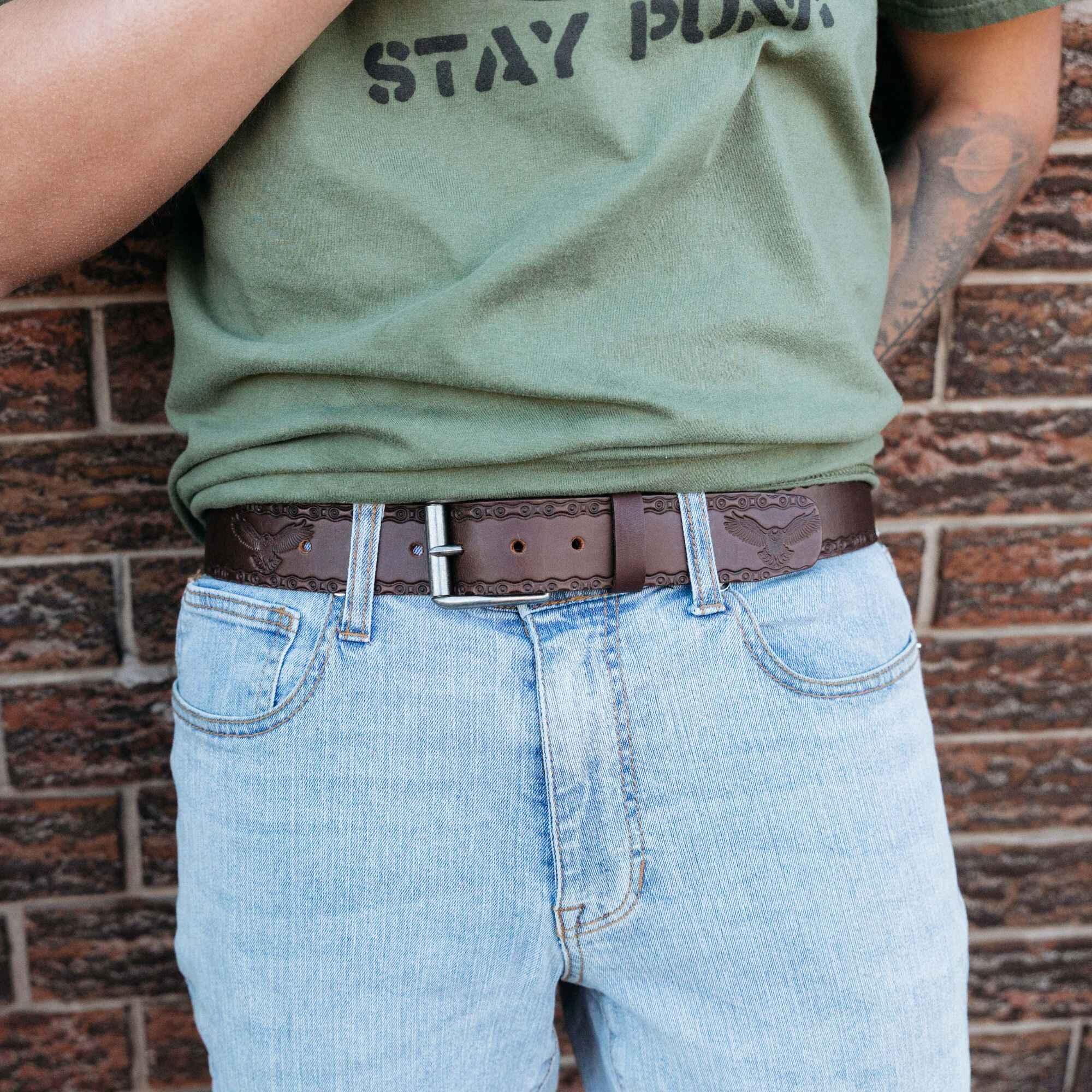 Person wearing light blue jeans, green Stay Punk shirt, and embossed brown leather belt