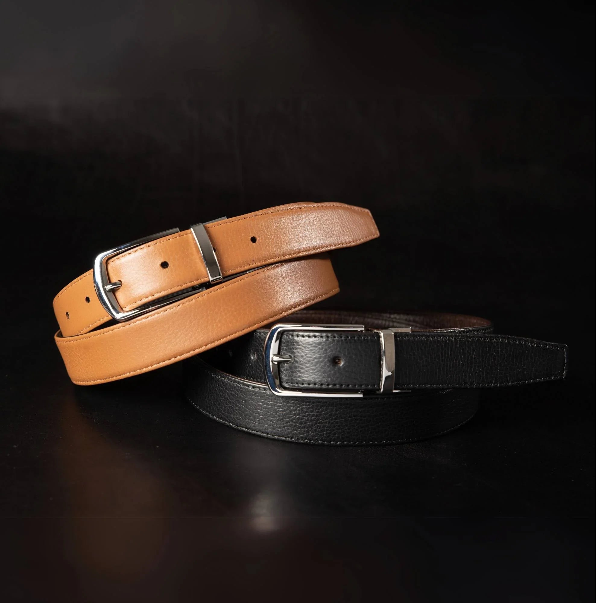 Tan and black leather belts with silver buckles on a black background