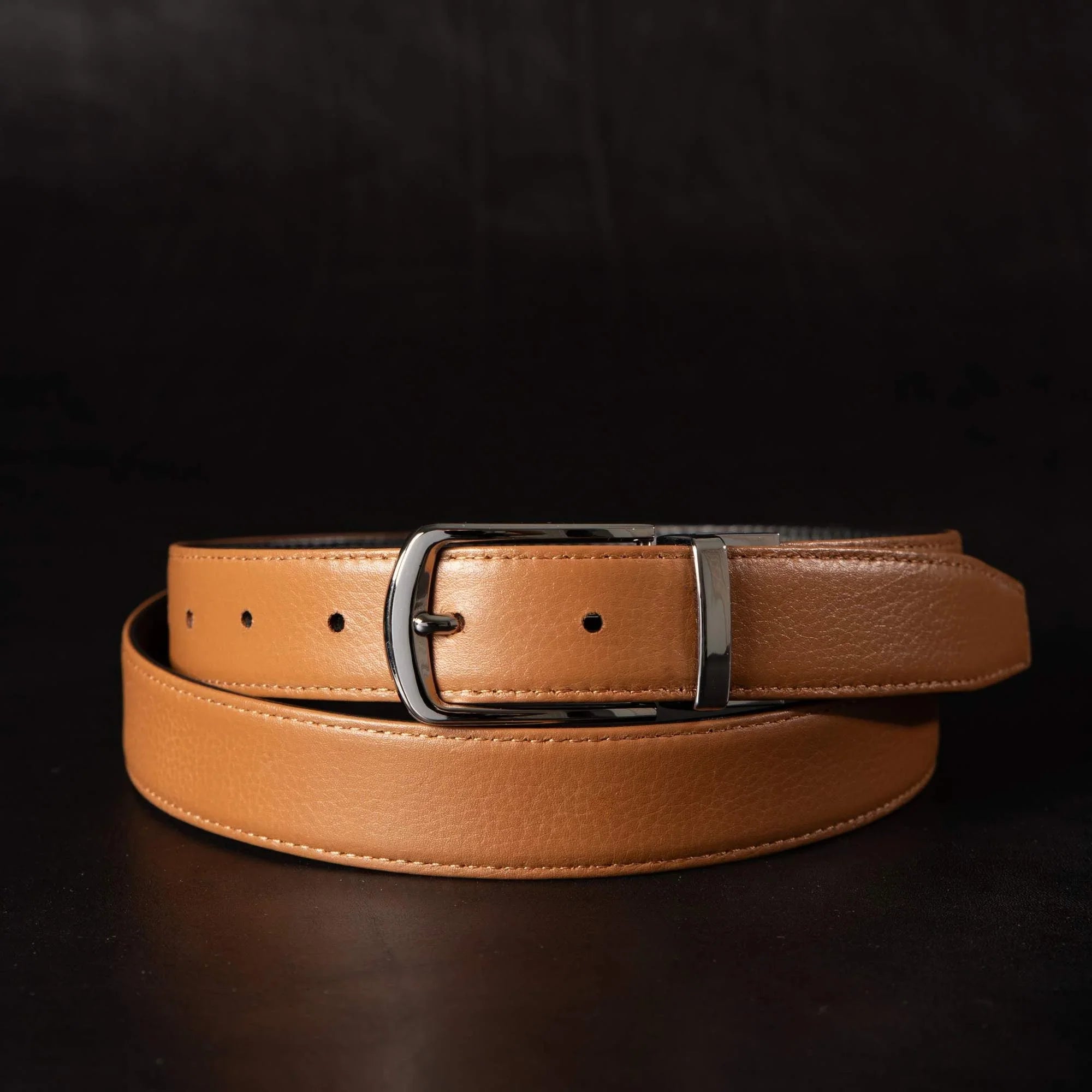 Tan leather belt with silver buckle on dark background