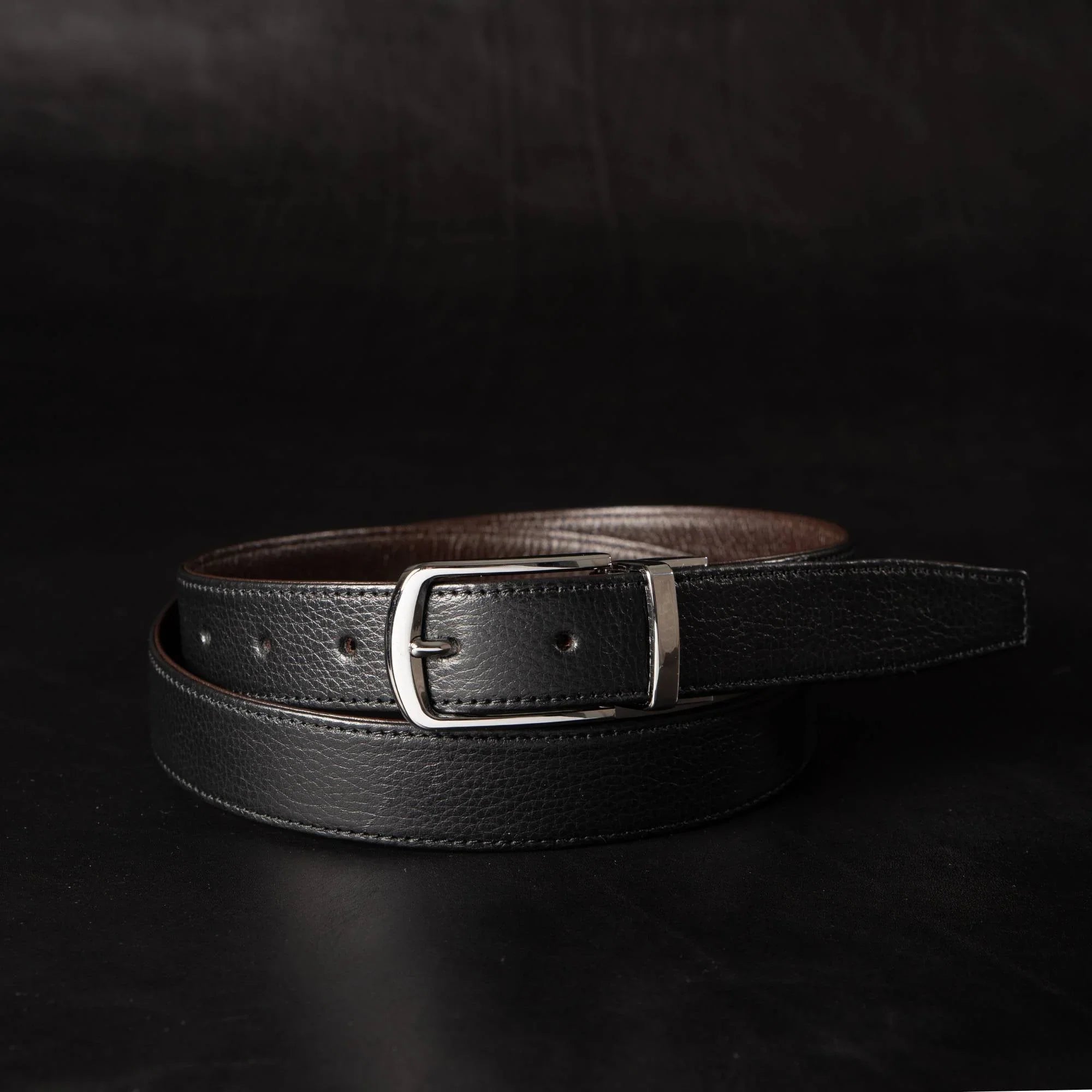 Black leather belt with silver buckle on dark background