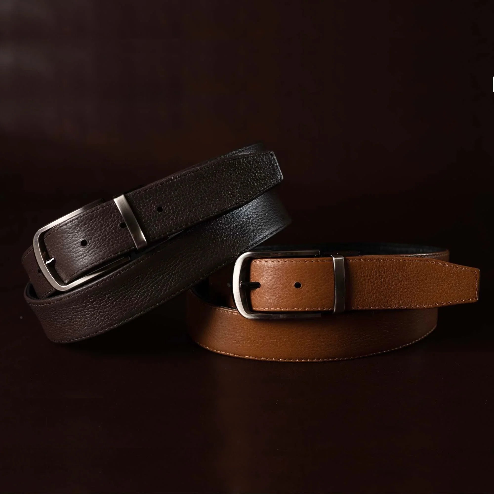 Brown and black leather belts with silver buckles on dark background