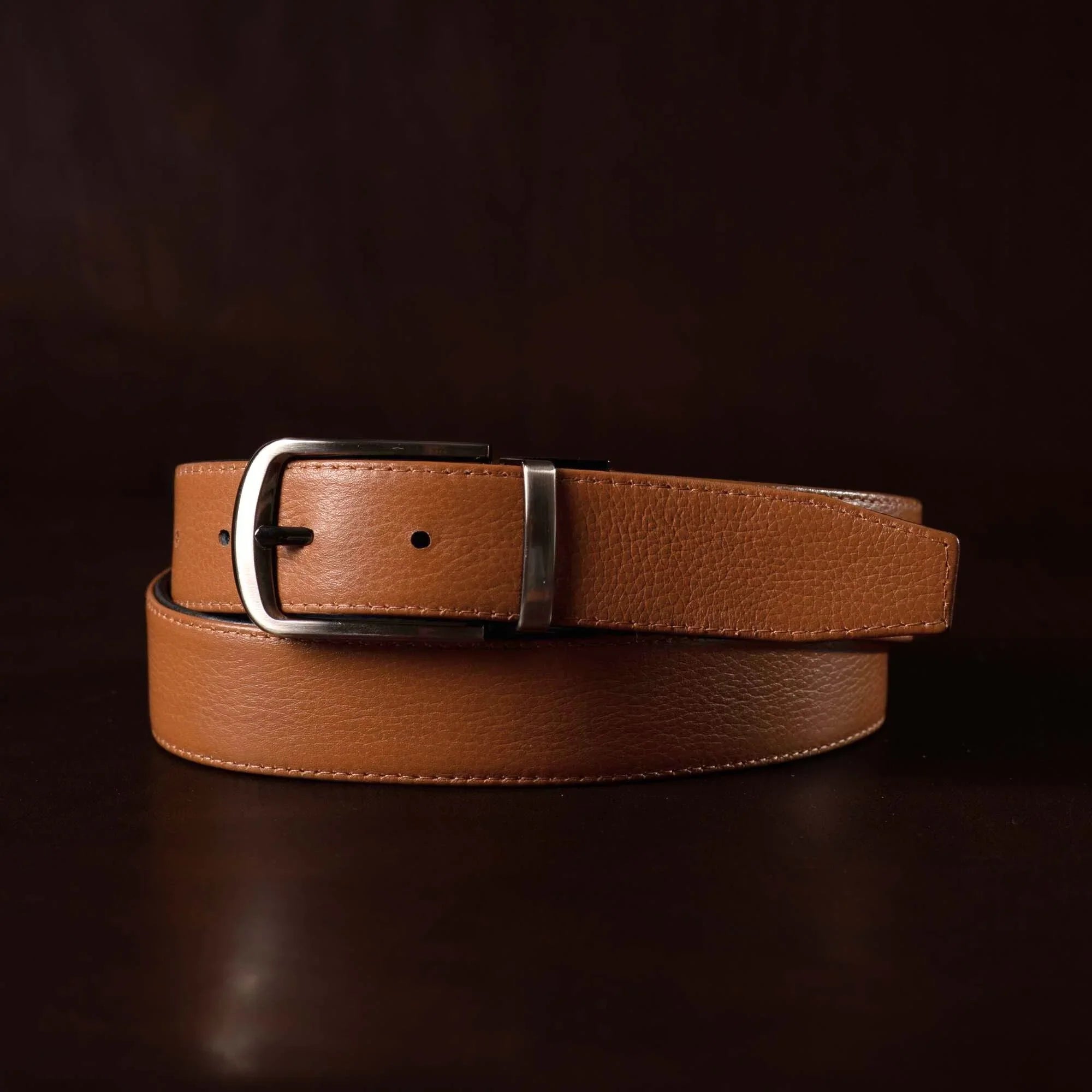 Brown leather belt with silver buckle on dark background