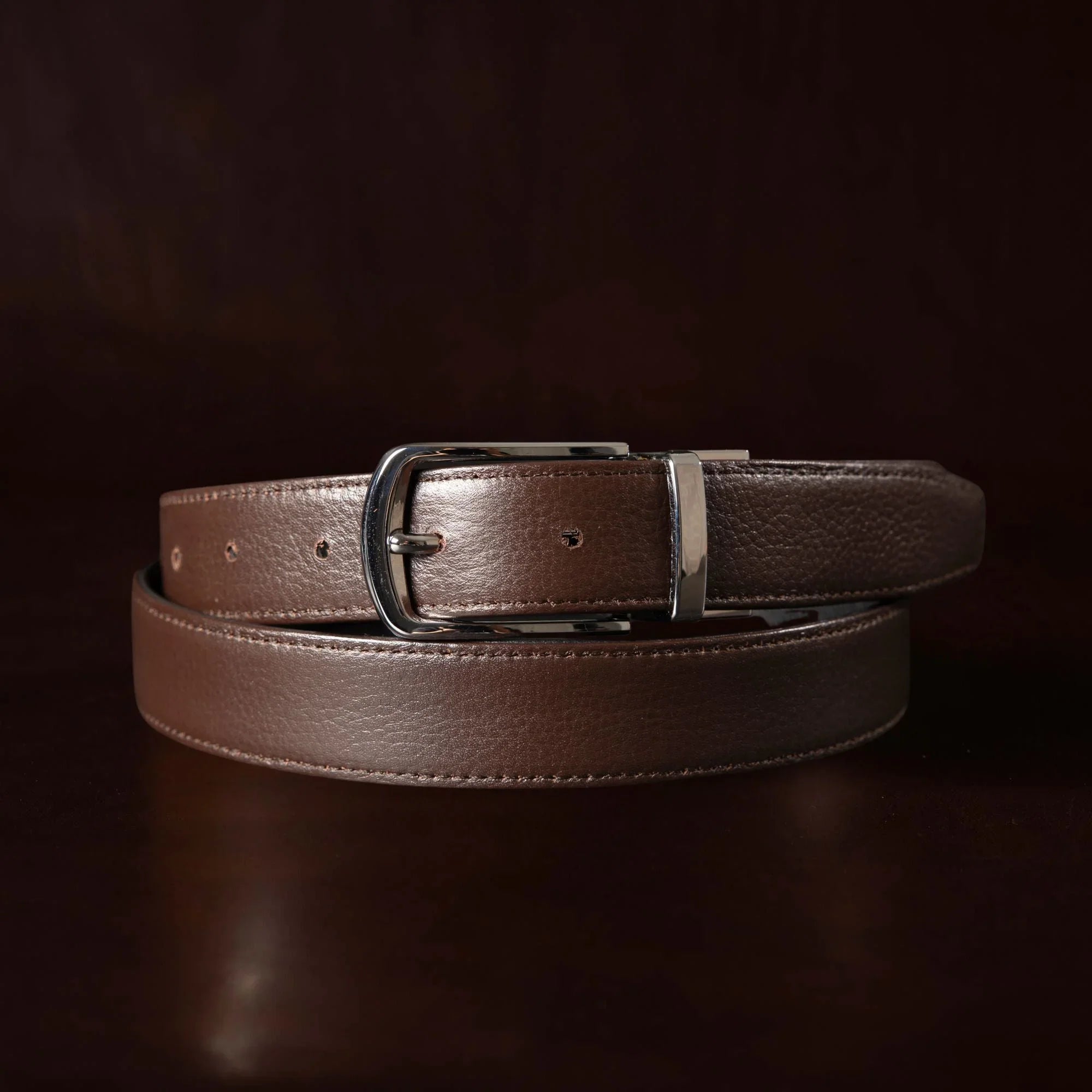 Brown leather belt with silver buckle on dark background