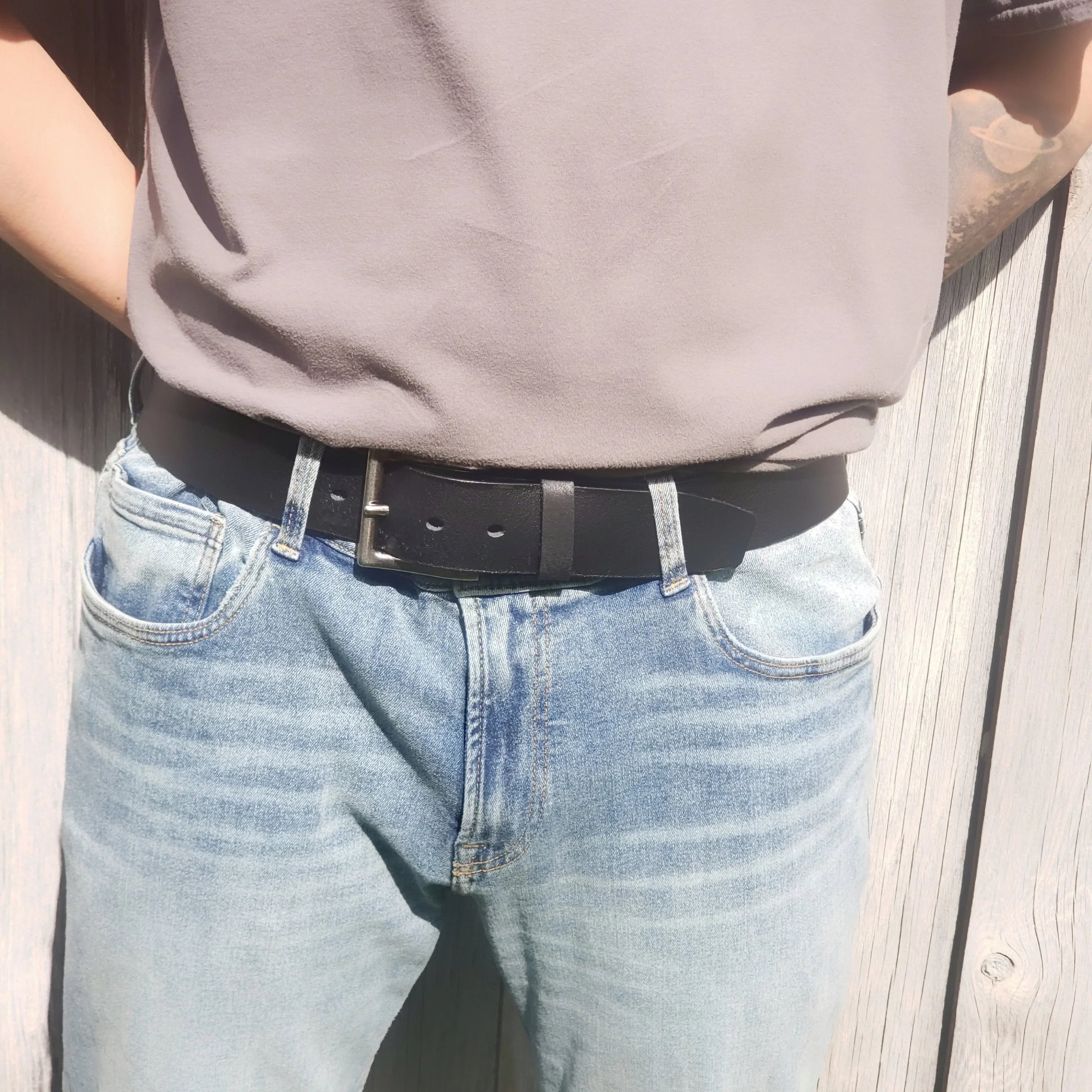 Black leather belt on light wash blue jeans and grey shirt outdoors