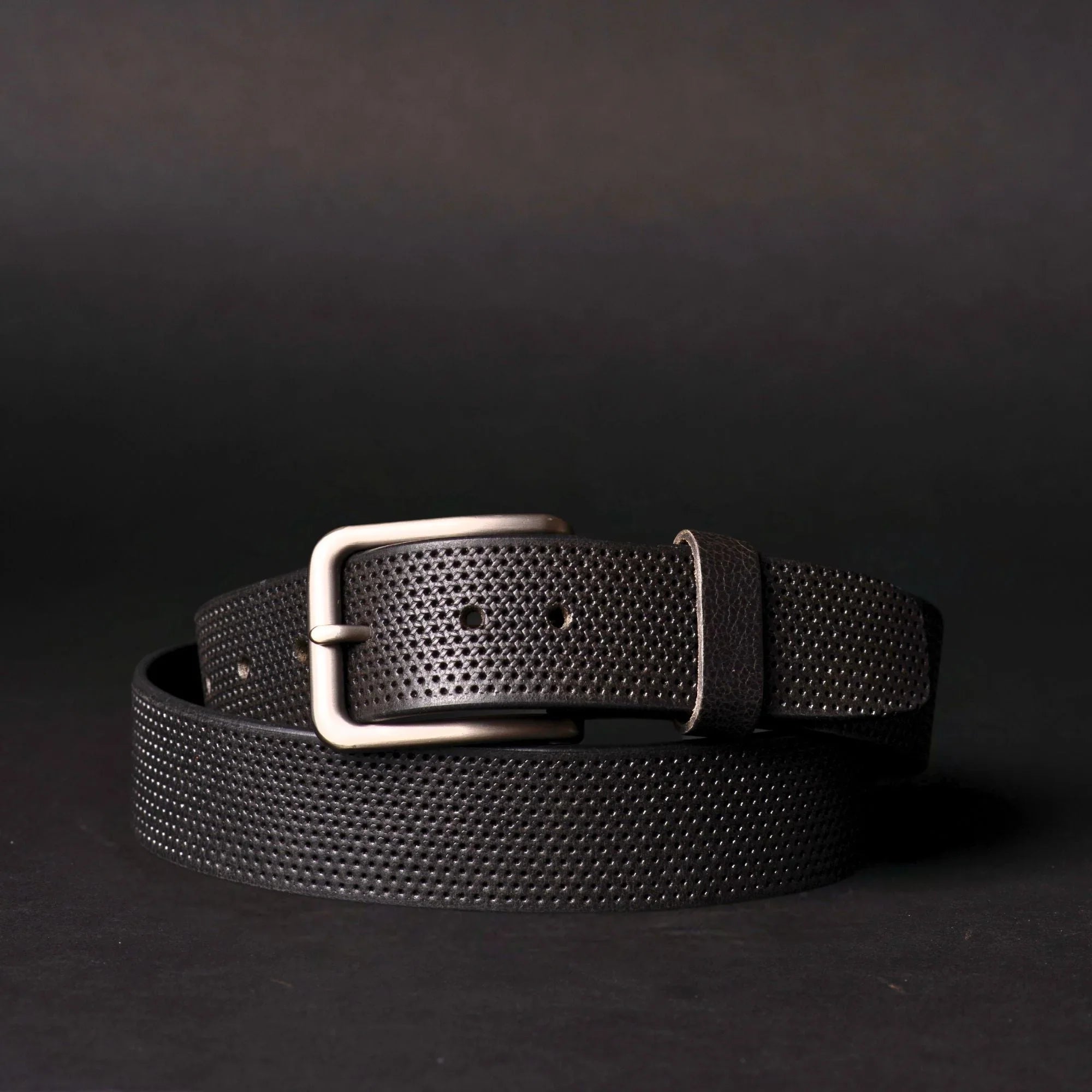 Black textured leather belt with silver buckle on dark background