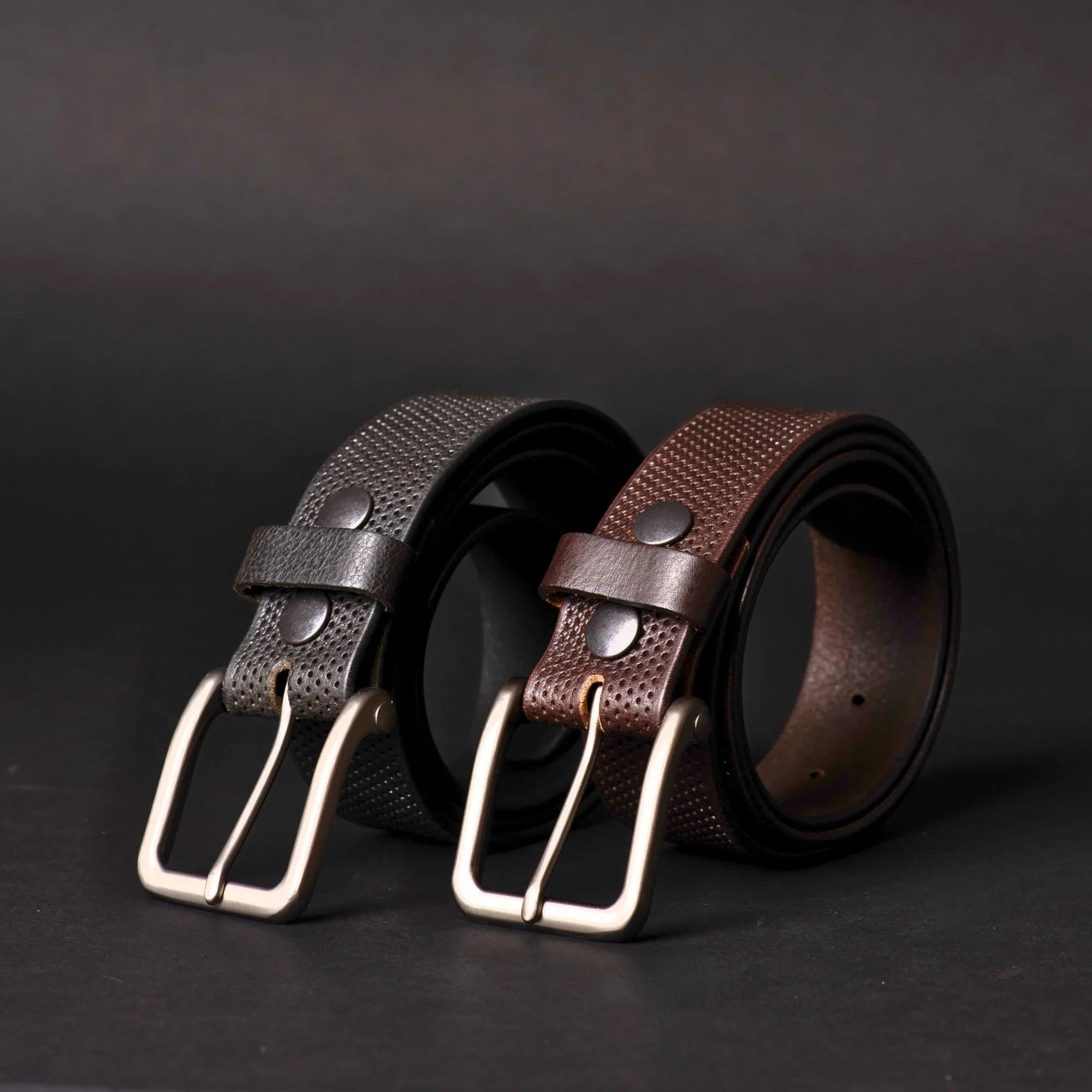 Black and brown textured leather belts with silver buckles on a dark background