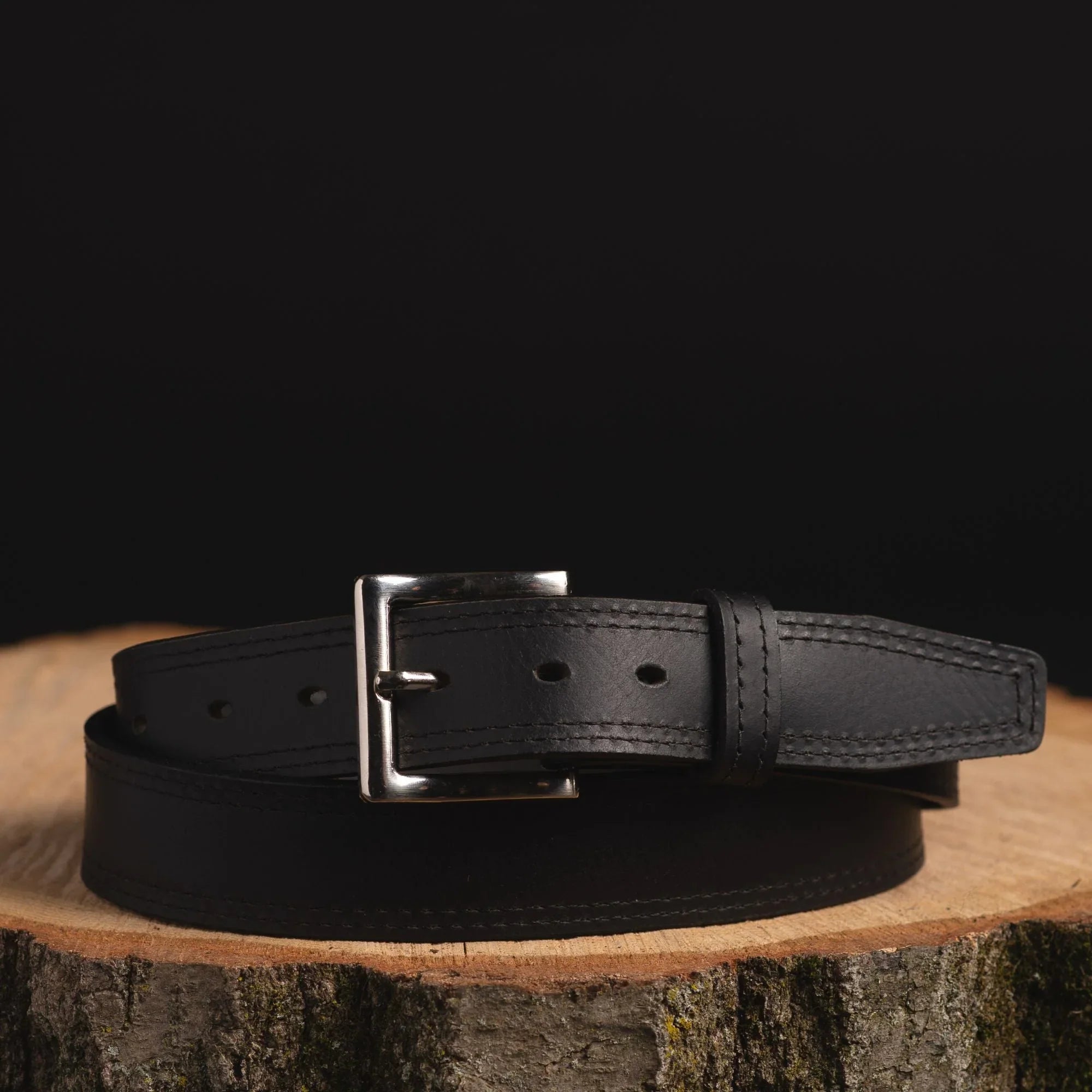 Black leather belt with silver buckle displayed on wood against black background