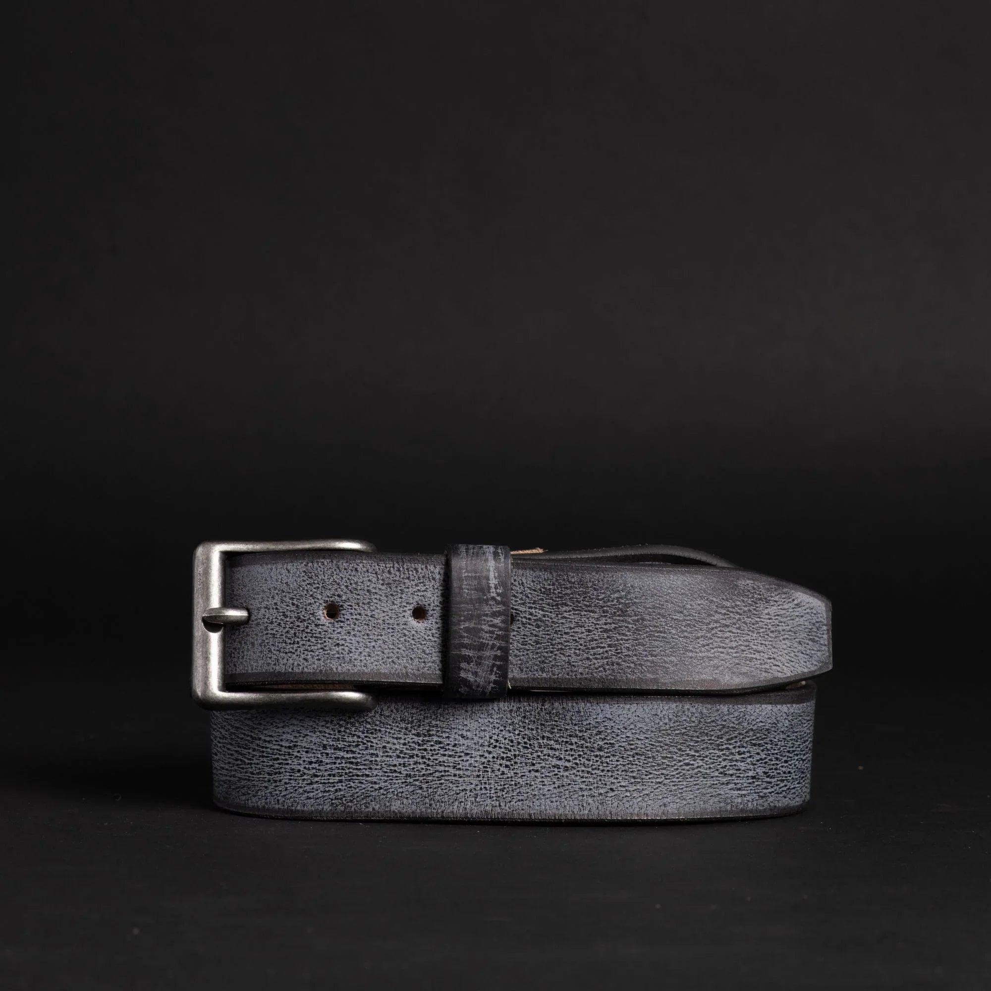 Textured black leather belt with silver buckle on black background