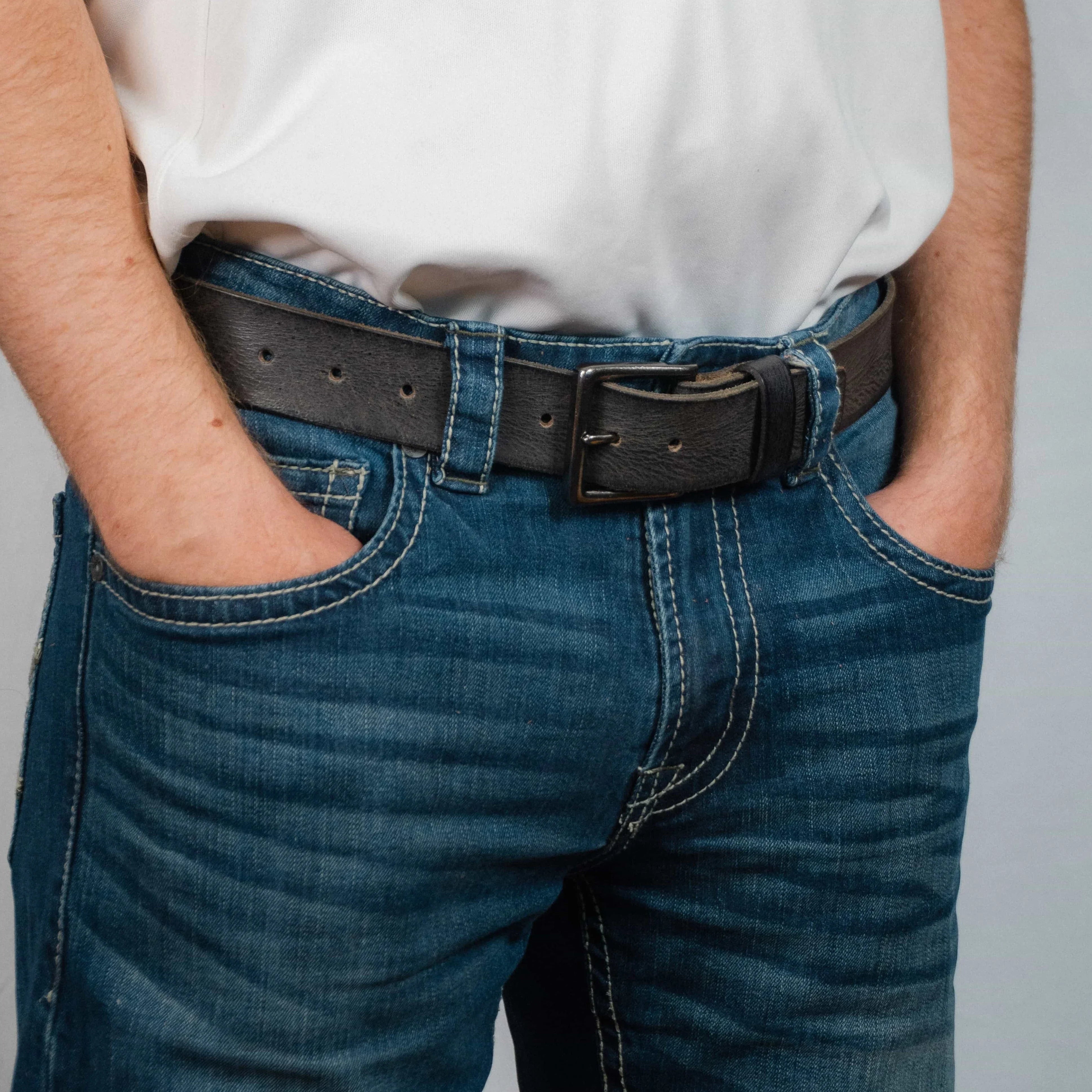 Man wearing blue jeans with a black leather belt and white shirt, hands in pockets