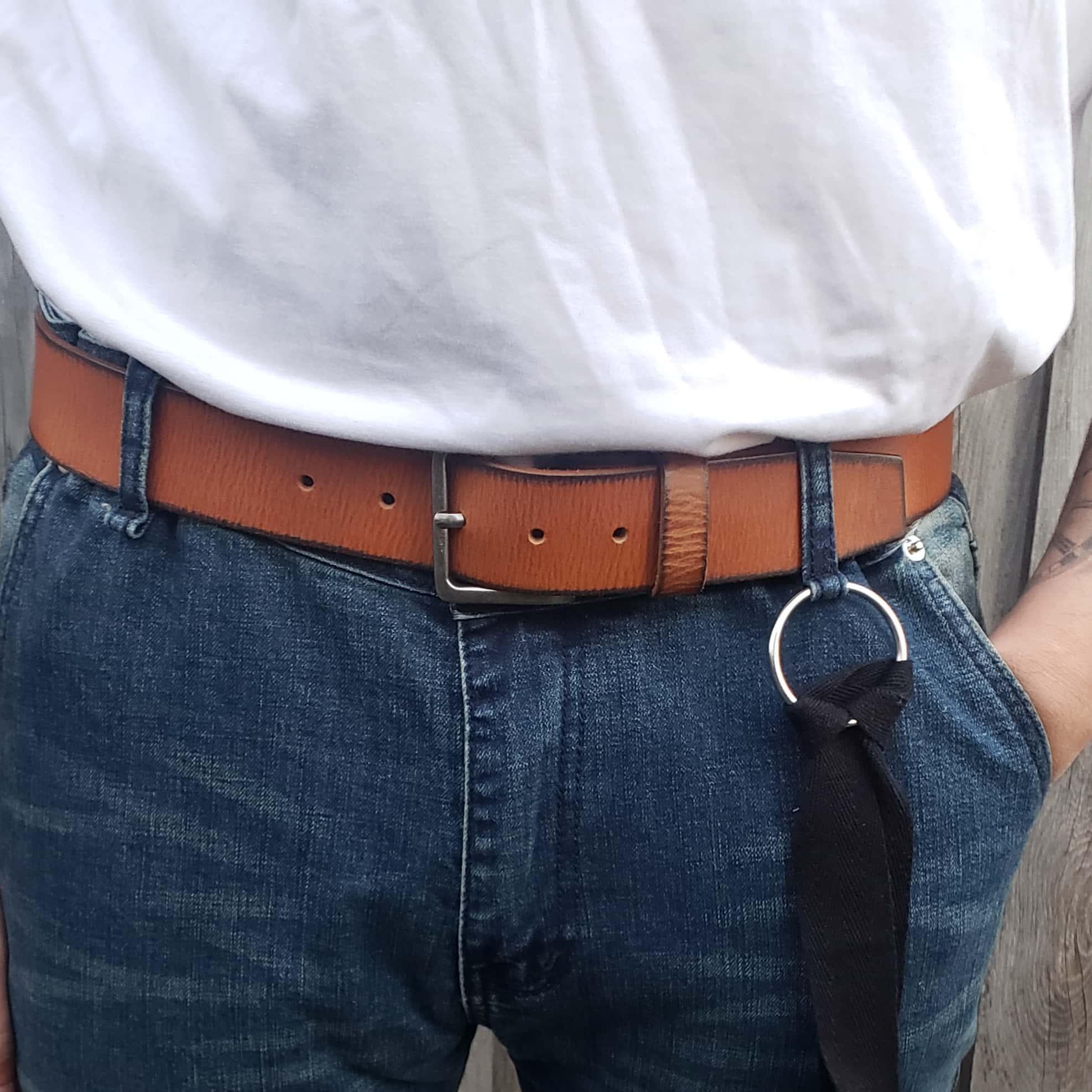 Brown leather belt with silver buckle on blue jeans and white shirt, black strap with ring
