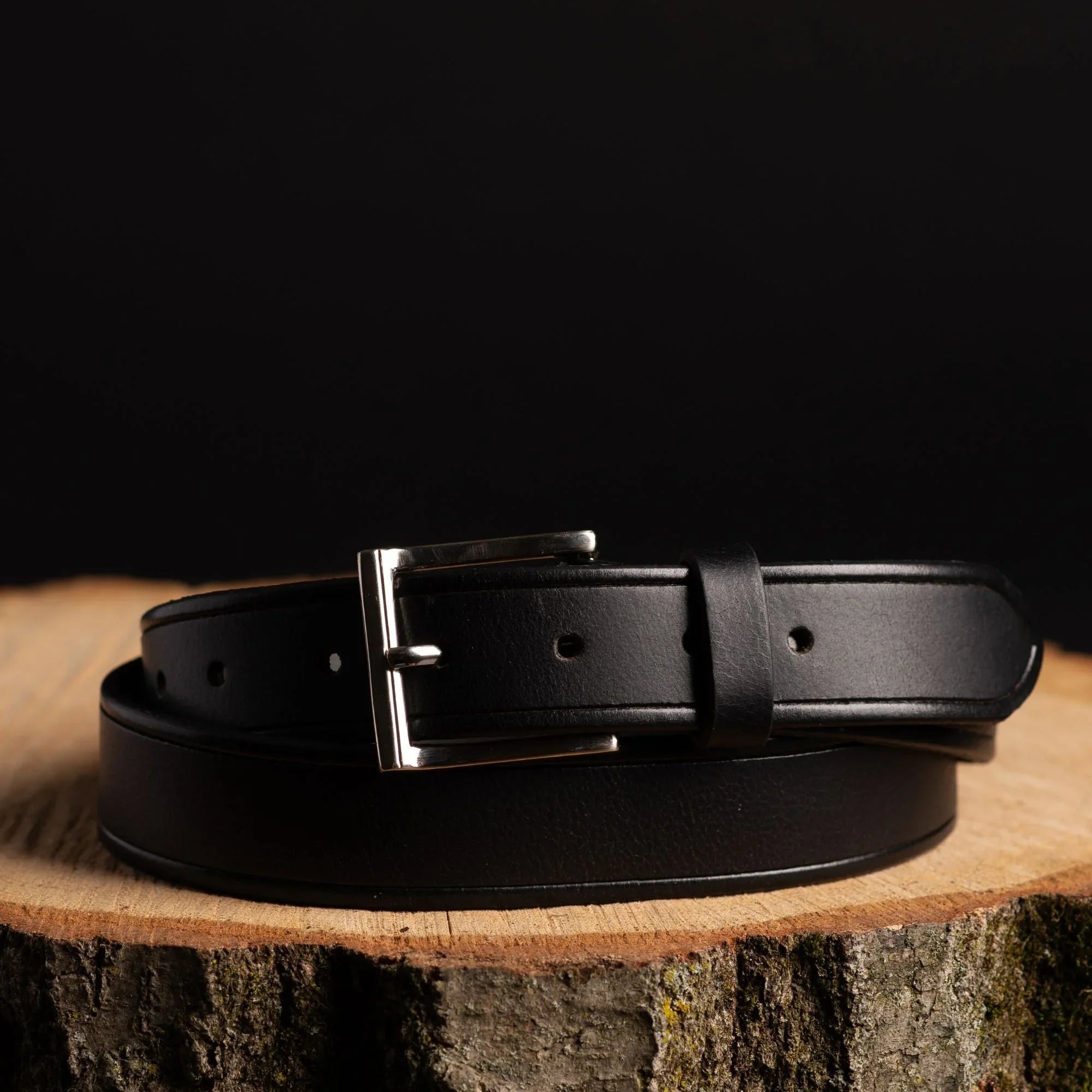 Black leather belt with silver buckle on wooden surface, fashion accessory product photo