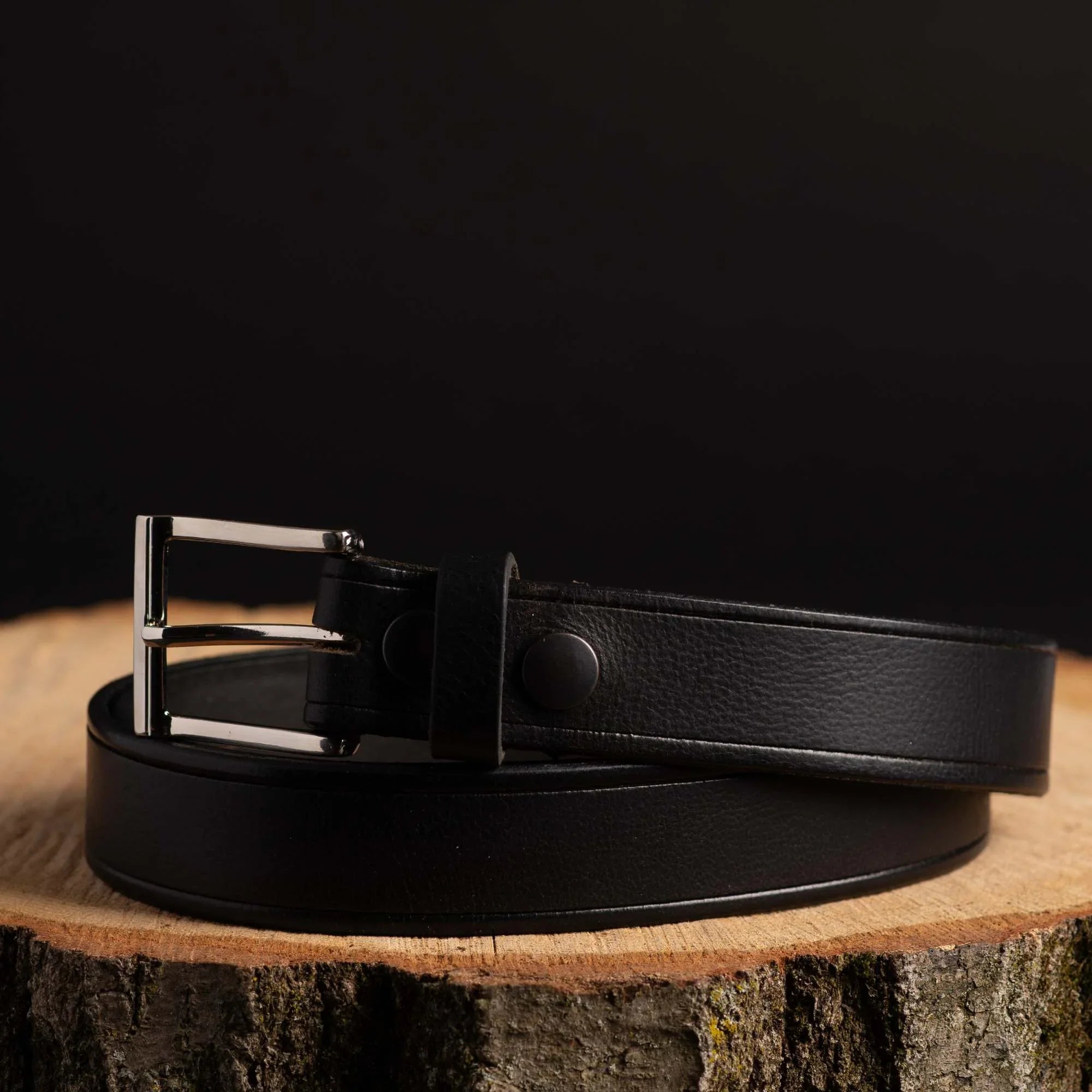 Black leather belt with silver buckle displayed on wooden surface, fashion accessory