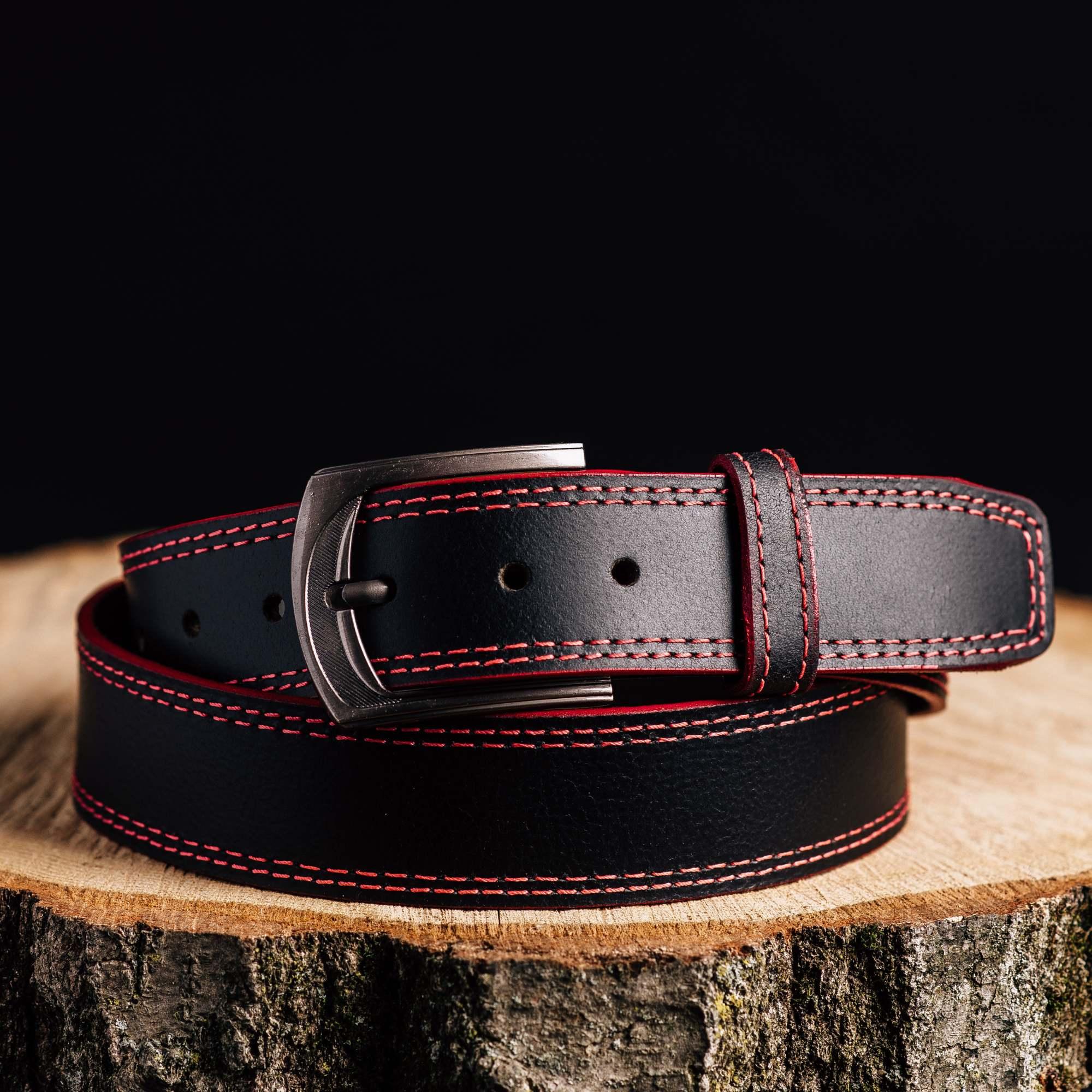Black leather belt with red stitching and metal buckle on wood stump, fashion accessory