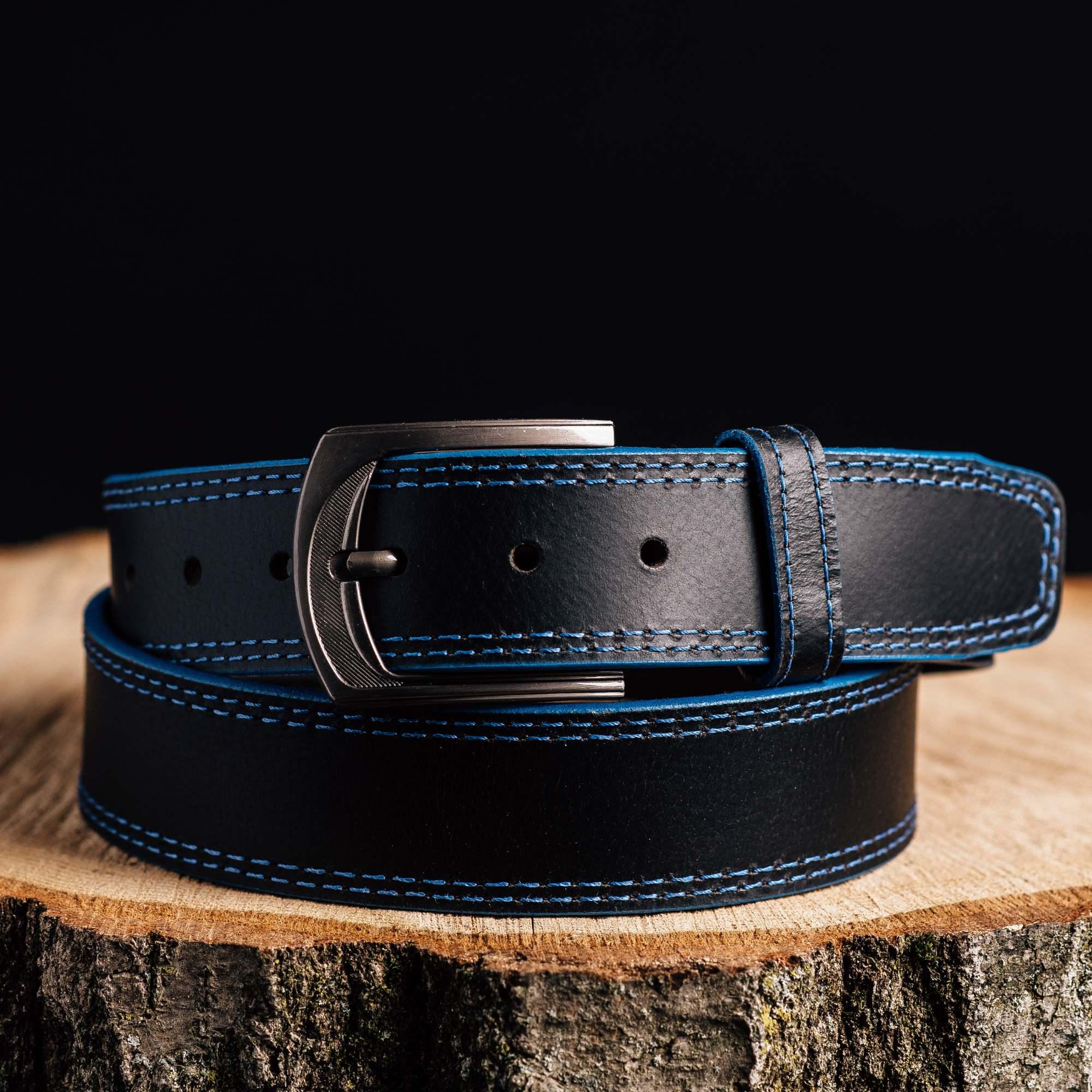 Black leather belt with blue stitching and metal buckle on a wooden stump