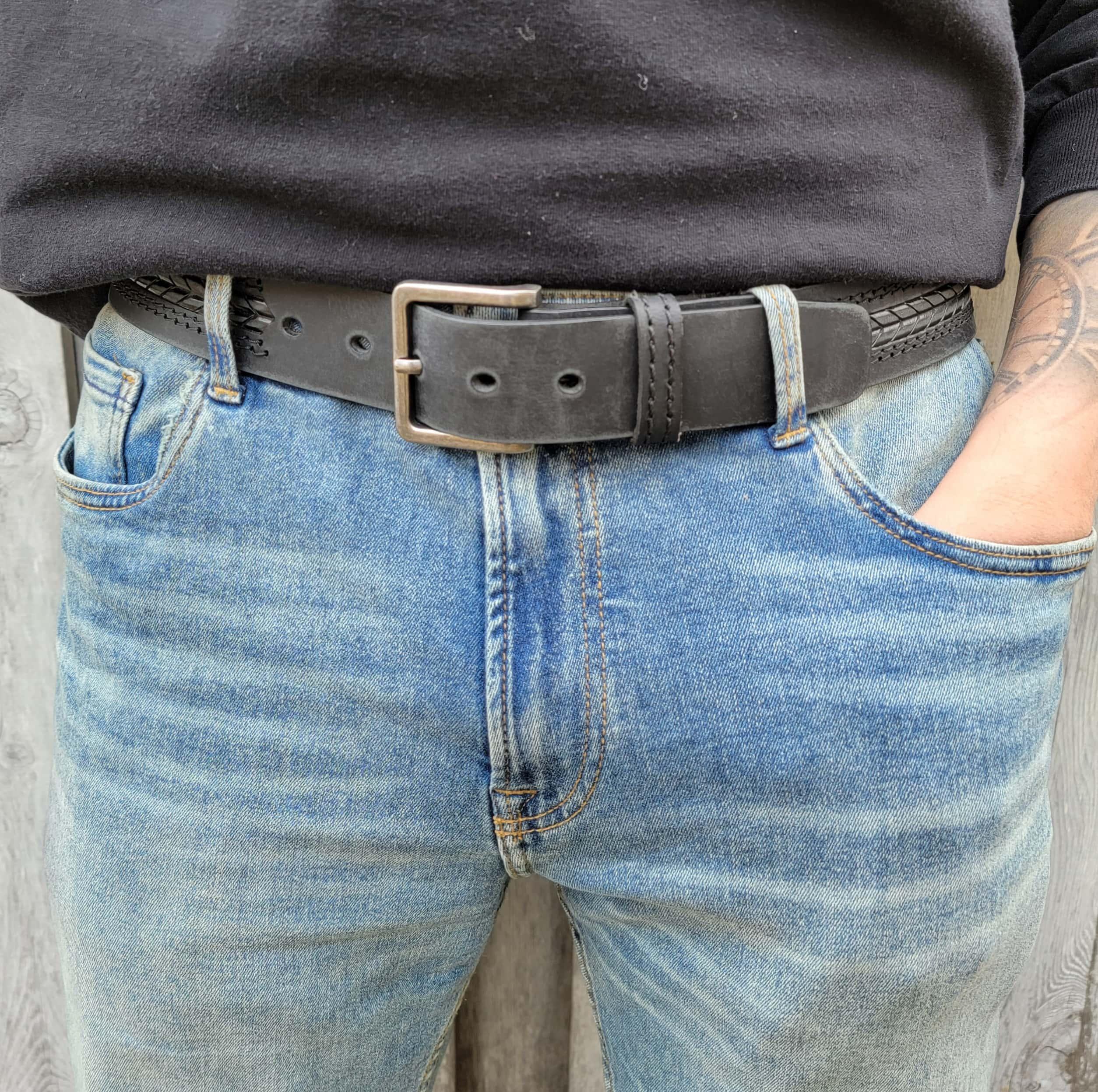 Close-up of black leather belt with metal buckle on blue jeans and black shirt