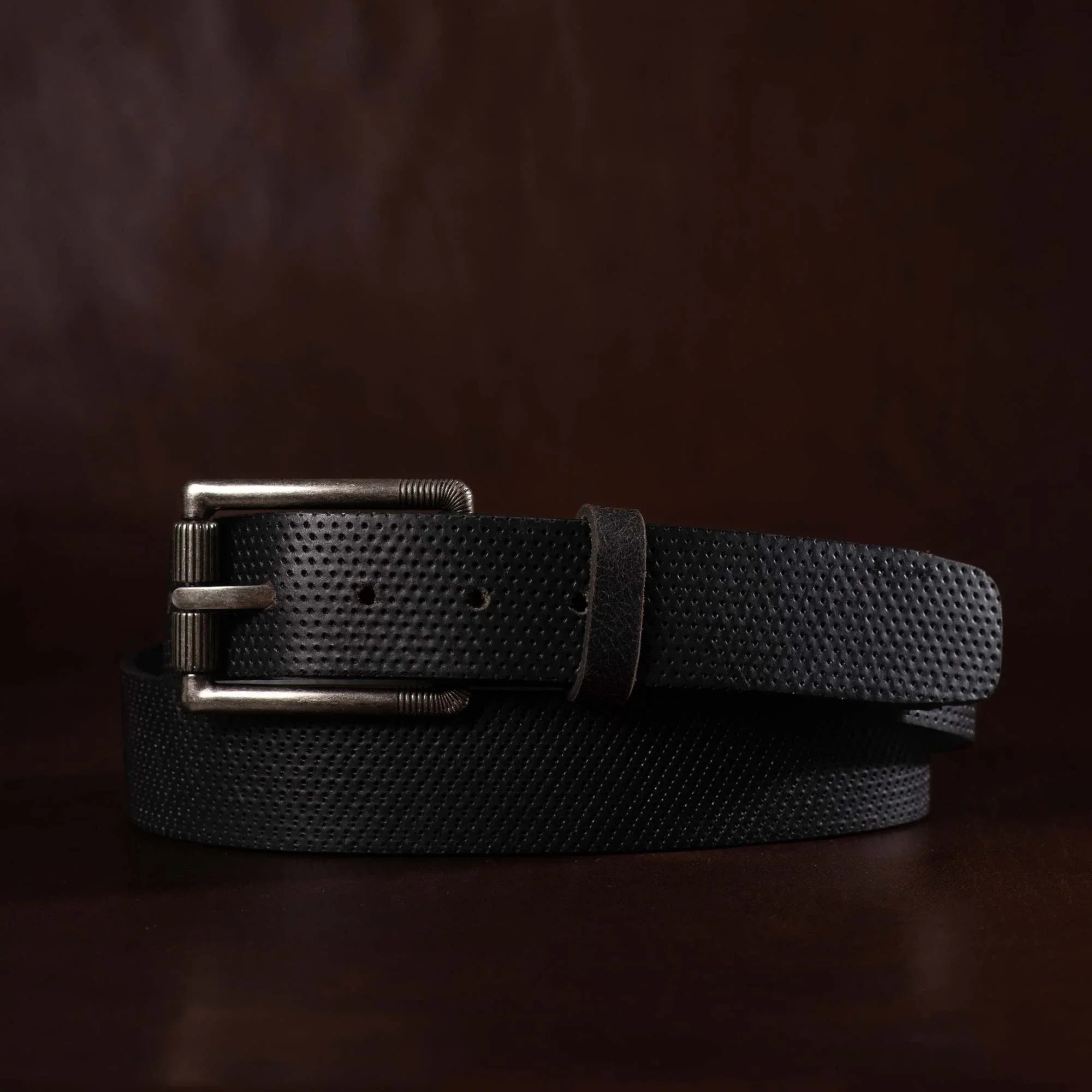 Black textured leather belt with silver buckle on dark brown background