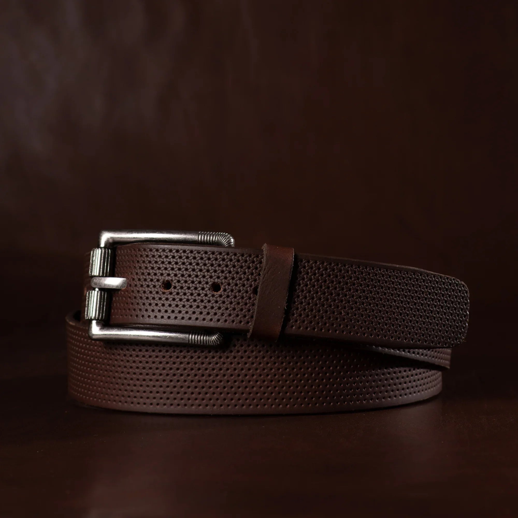 Textured brown leather belt with silver buckle on dark background