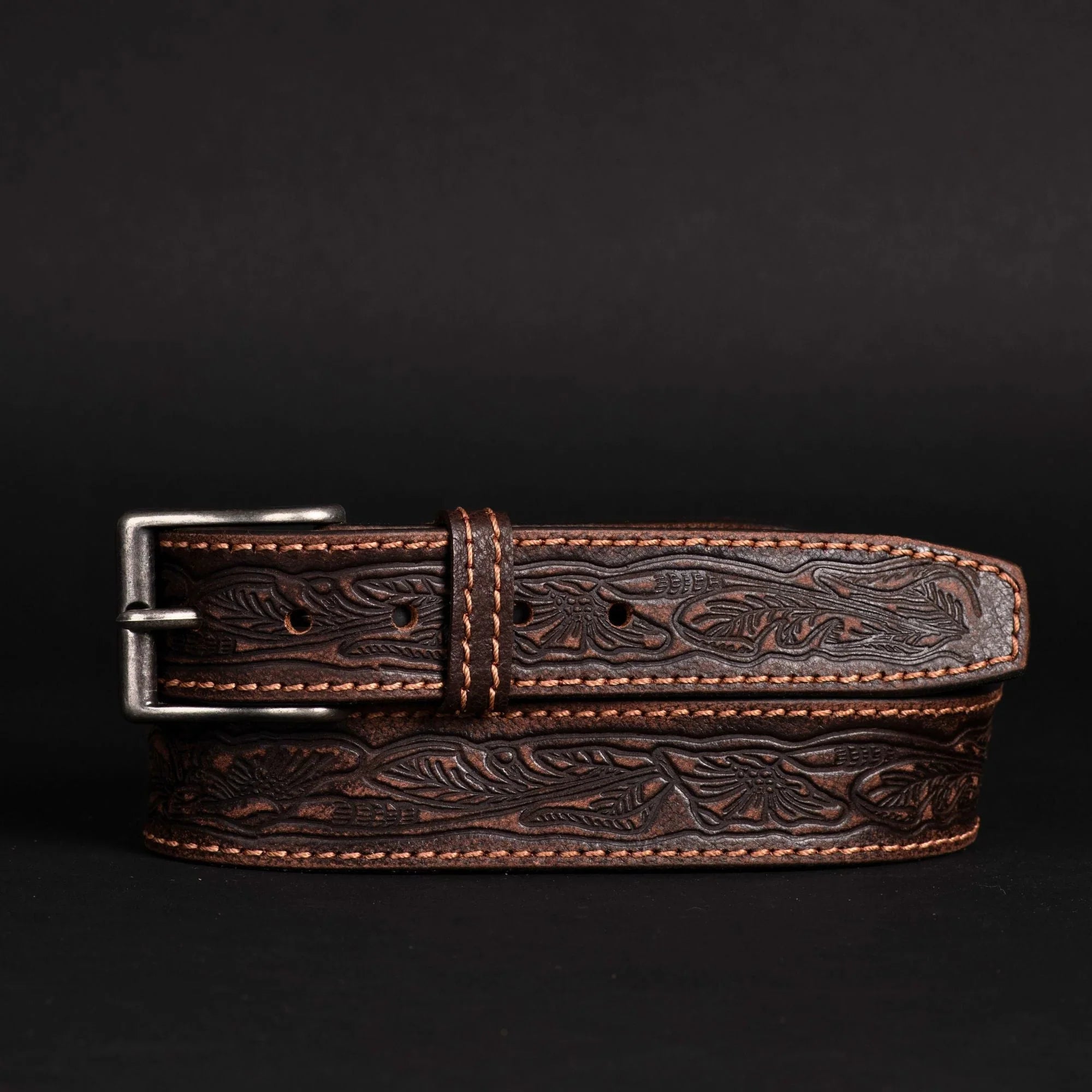 Hand-tooled brown leather belt with floral pattern and silver buckle on black background