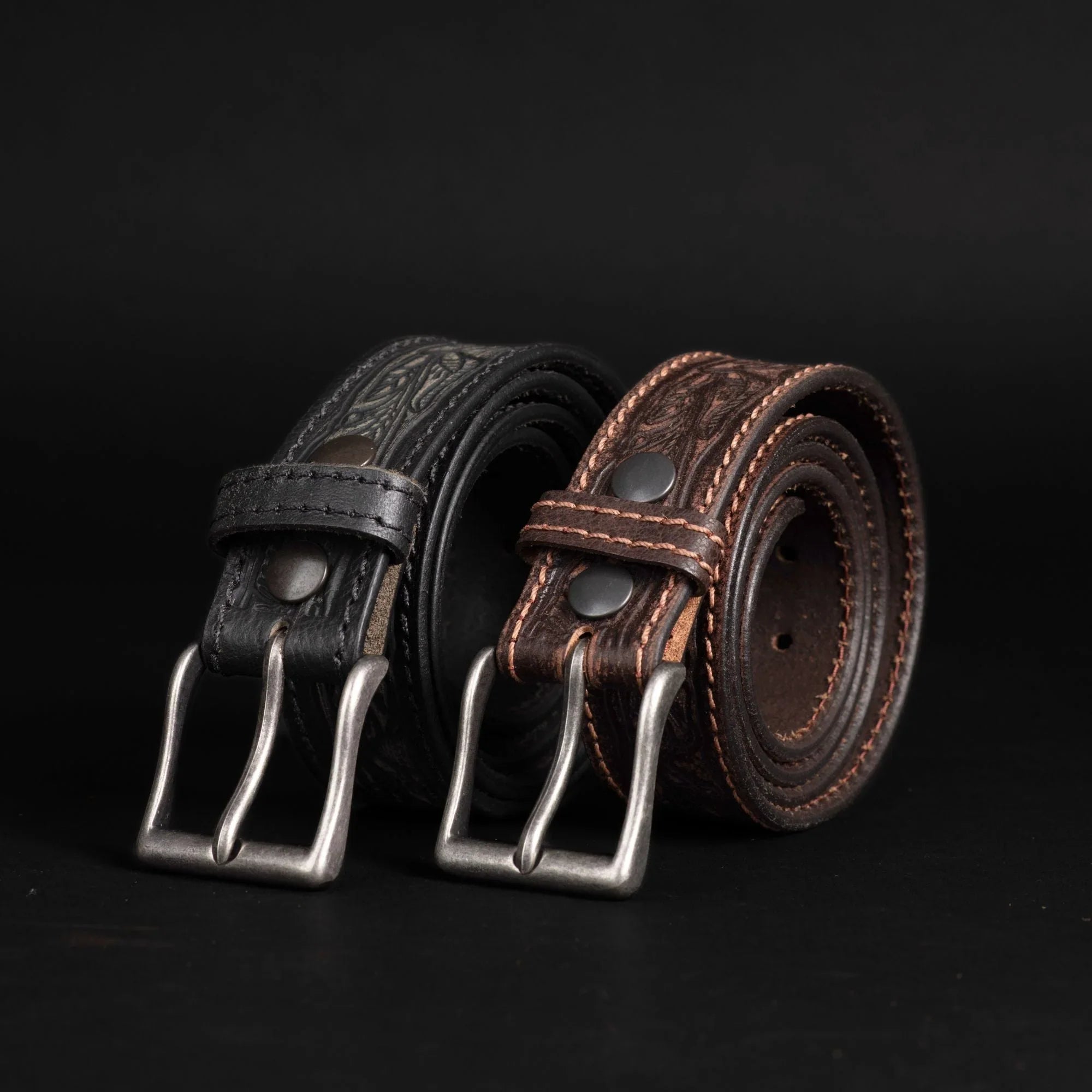 Black and brown embossed leather belts with metal buckles on black background