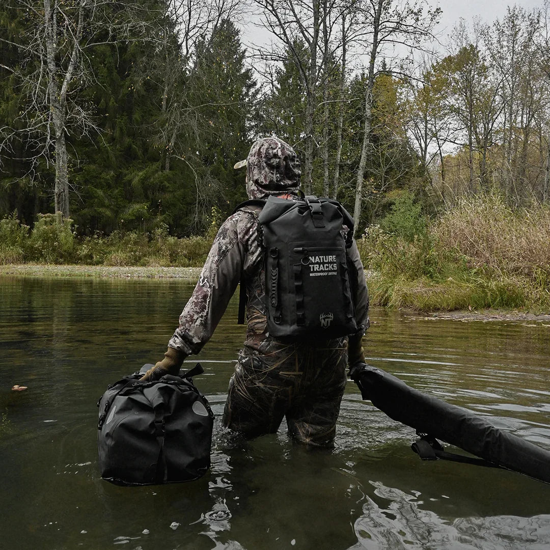 Hunter in camouflage gear wading through water with Nature Tracks waterproof backpack and gear bags