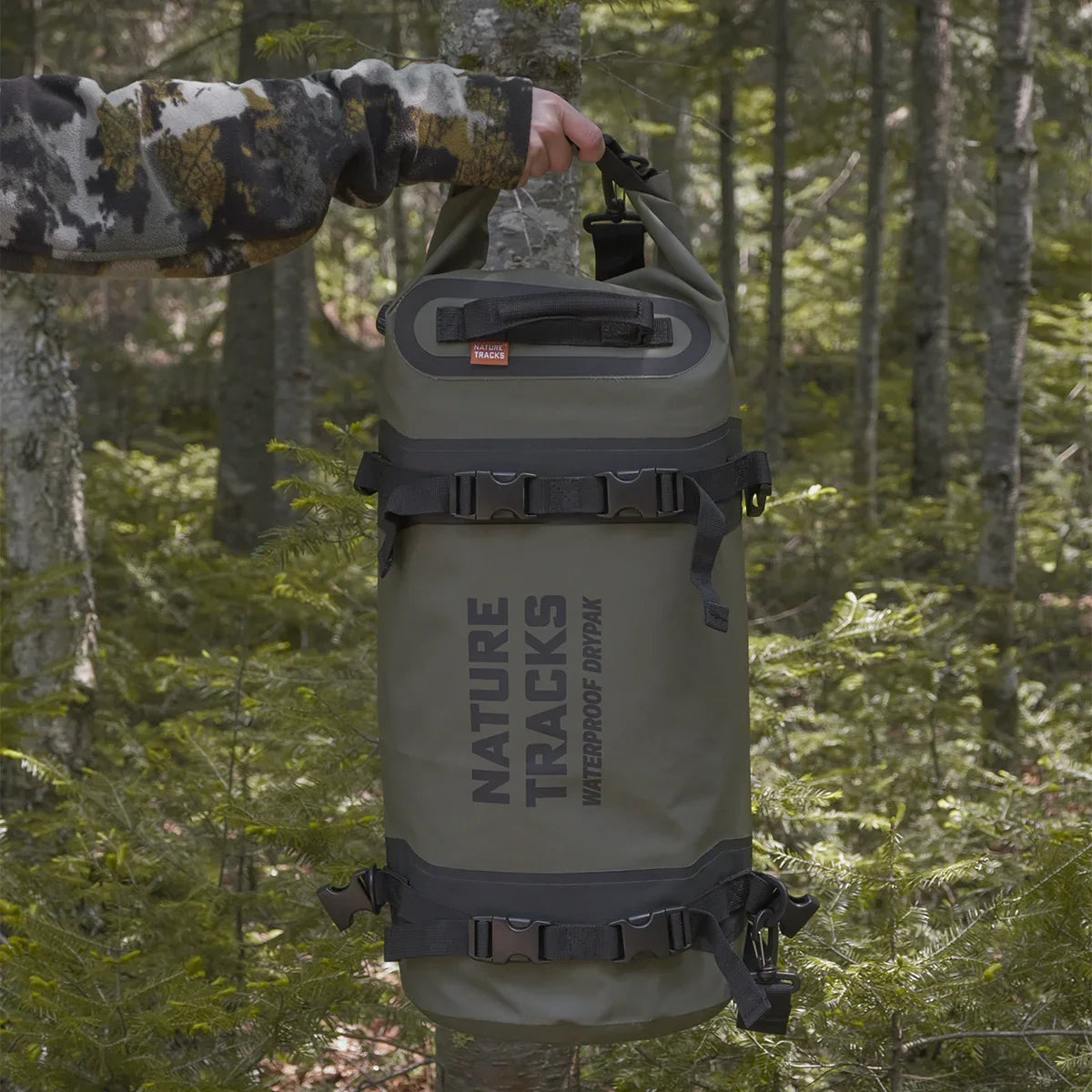 Green waterproof Nature Tracks duffel dry bag held in forest, outdoor gear for hiking.