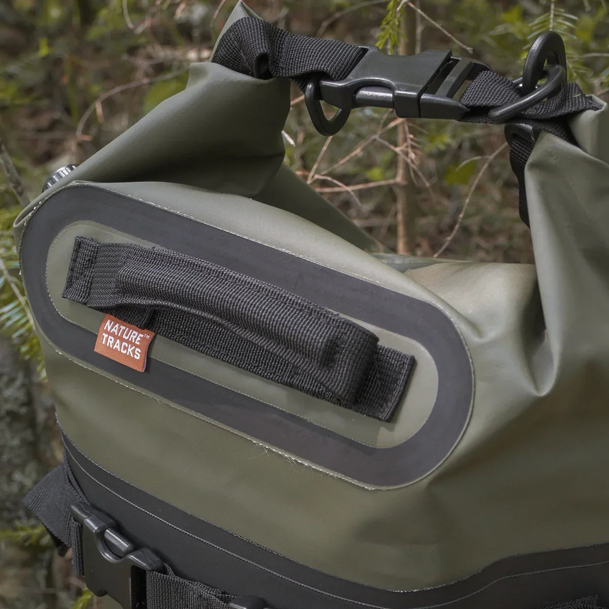 Olive green Nature Tracks waterproof duffel bag with black strap in a forest setting